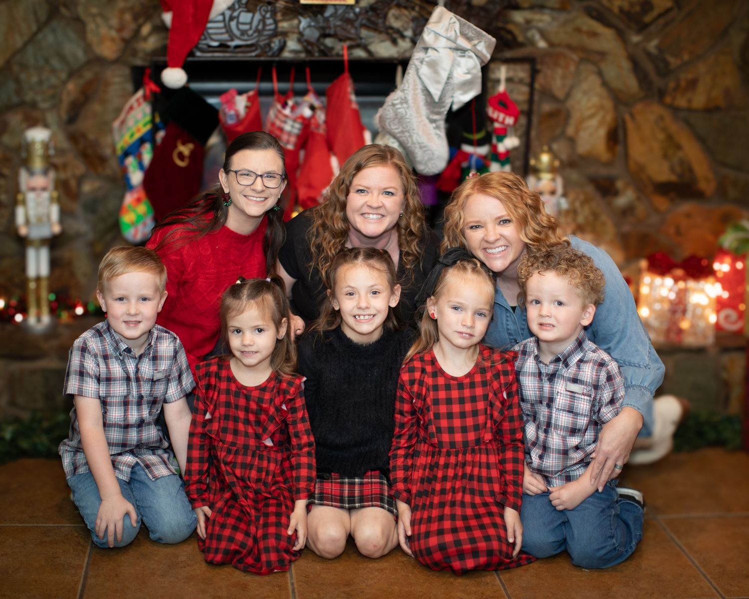 Family group wearing coordinated red plaid and blue outfits poses together for holiday photos in rustic setting.