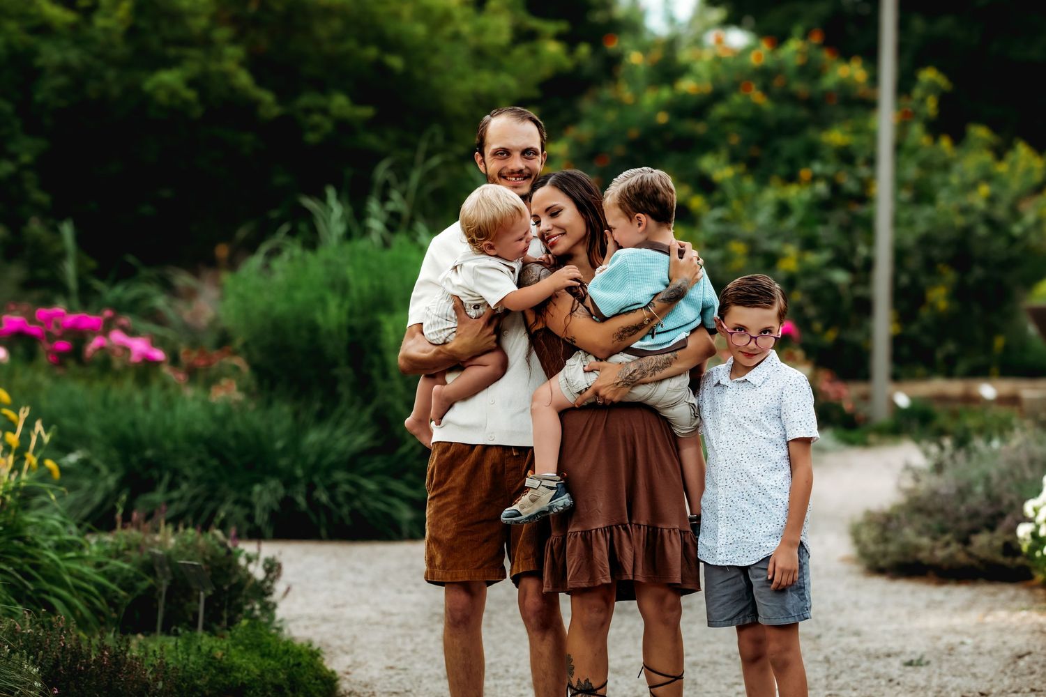 A group of people share tender moments together in a garden setting during a sunny outdoor photoshoot.
