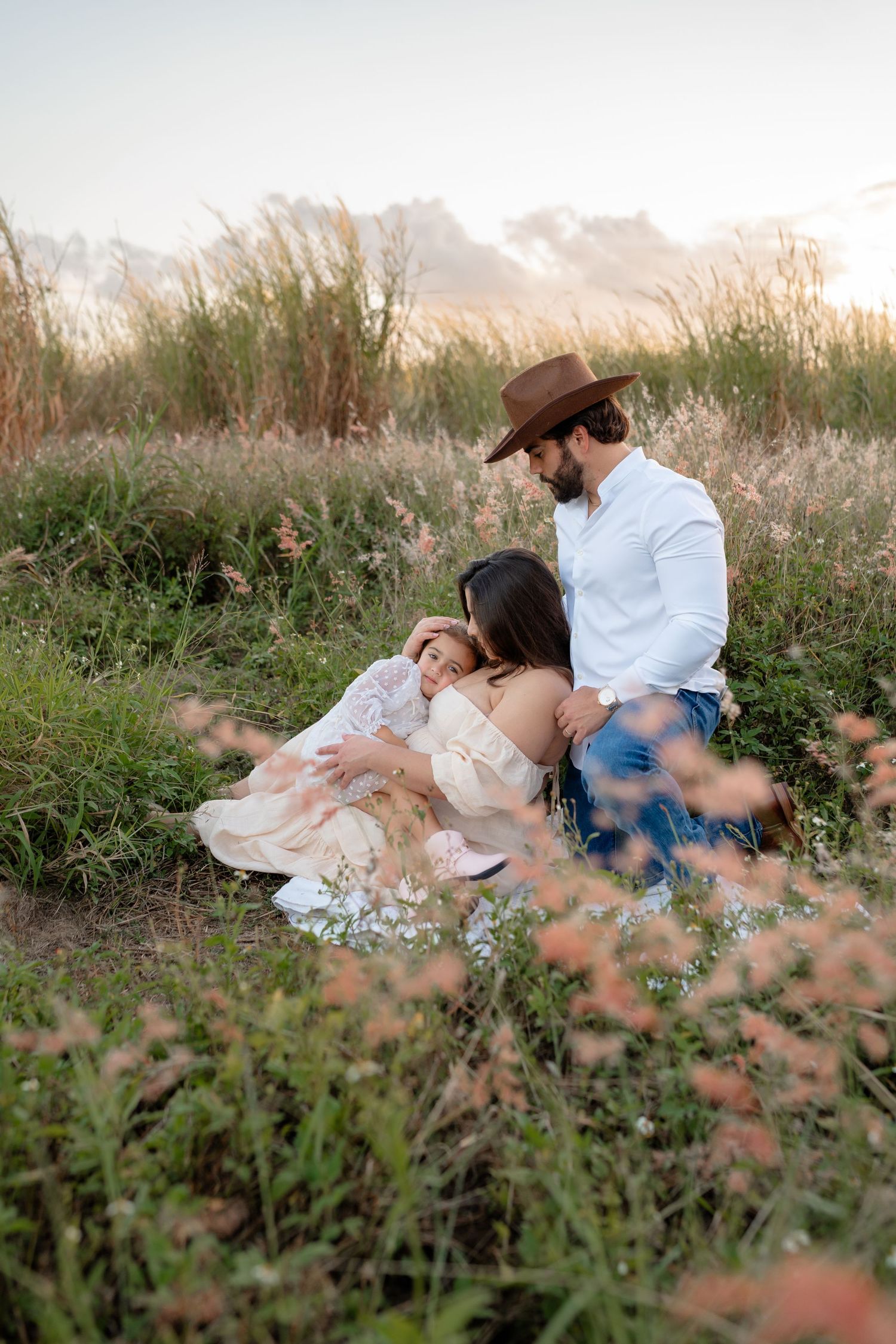 A couple relaxes together in a wildflower meadow at sunset, surrounded by tall grass and soft natural light.
