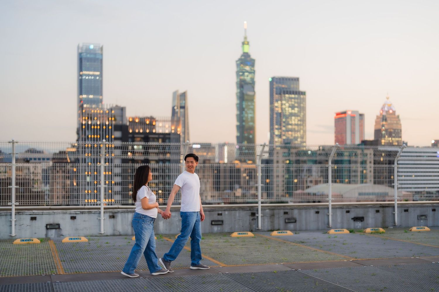 People walking on a rooftop parking deck with city skyline views at sunset.