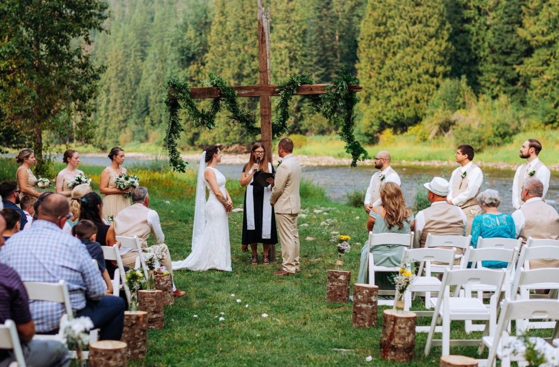 Outdoor wedding ceremony setup in a lush forest setting with white chairs and natural greenery backdrop.