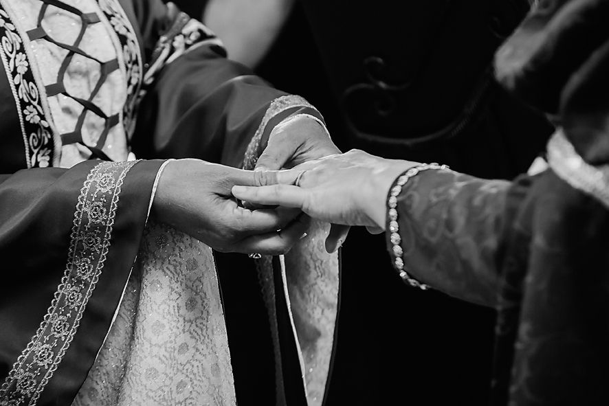 Black and white close-up of hands exchanging rings during a traditional Indian wedding ceremony.