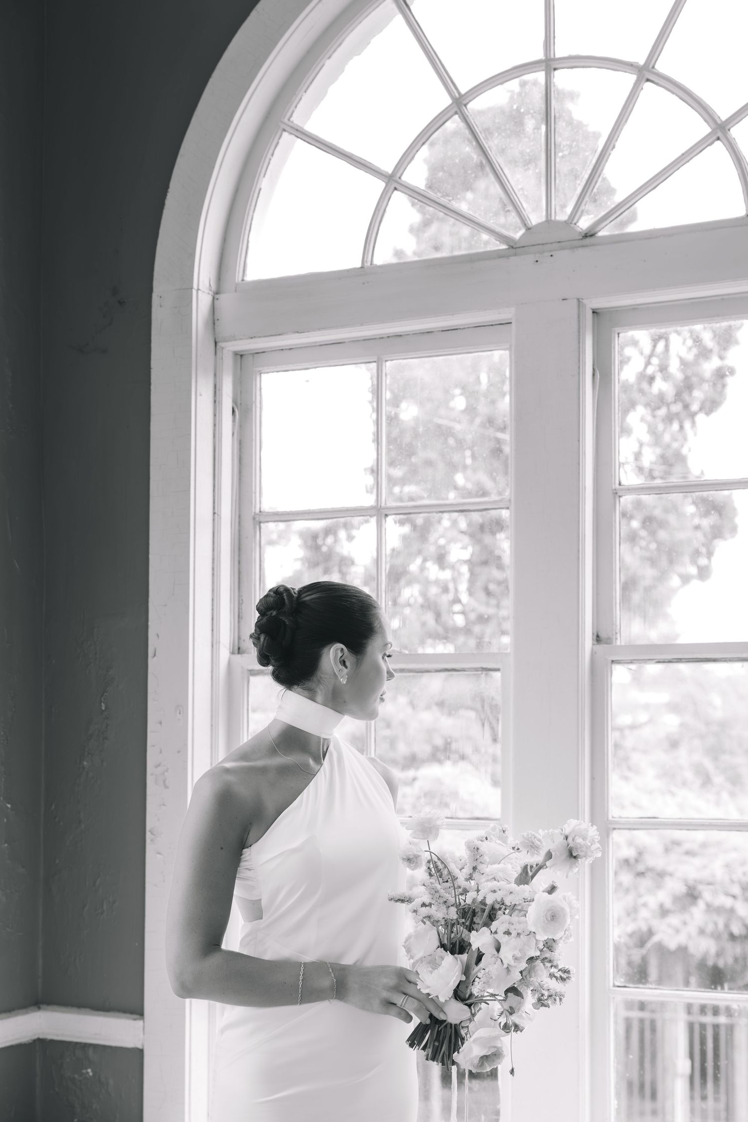 A classic black and white wedding photograph showing someone in a white dress by arched windows with natural light streaming in. Knoxville.