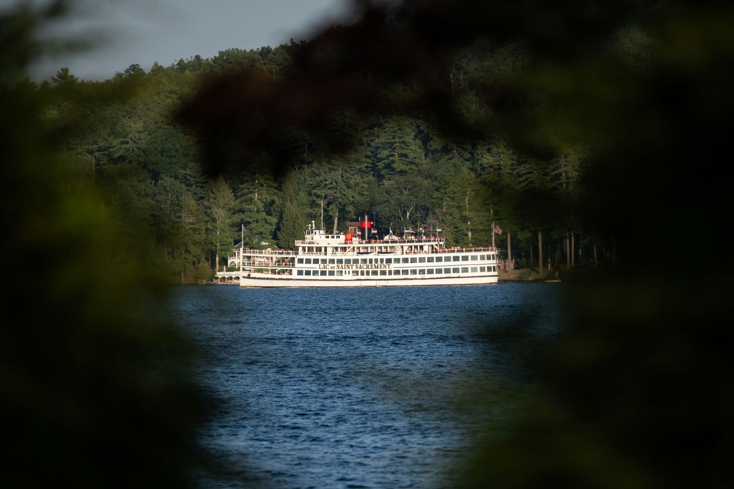 A white passenger ferry boat cruises across blue waters with forested shoreline visible in the background.