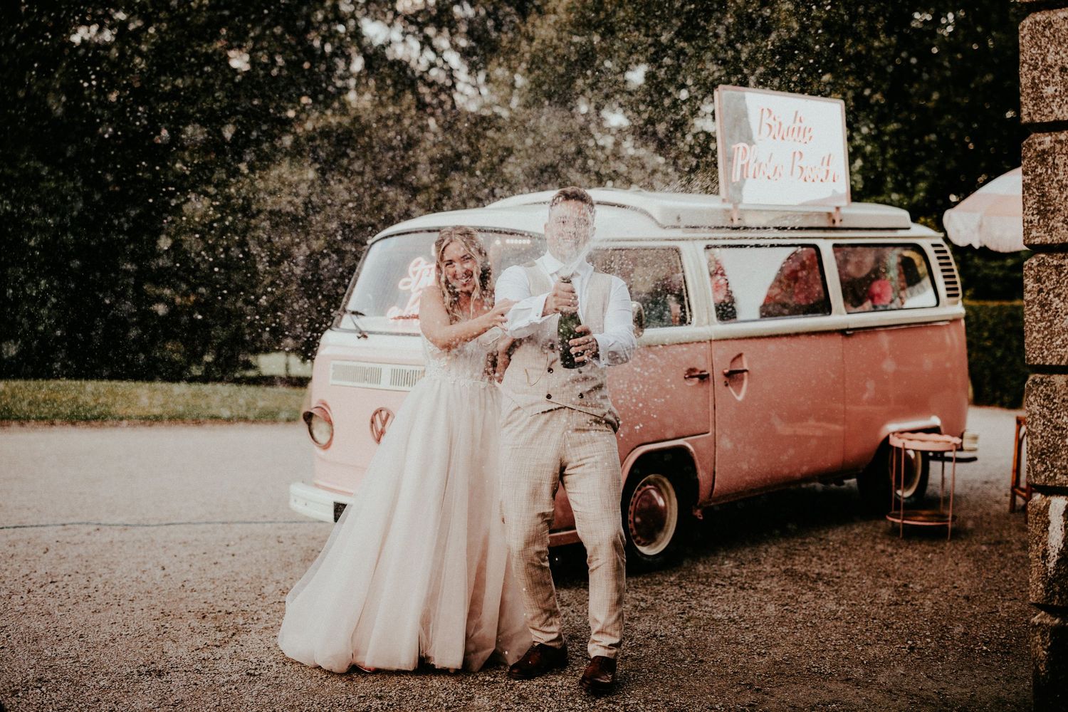 Vintage coral VW bus serves as backdrop for wedding couple in romantic outdoor photoshoot.