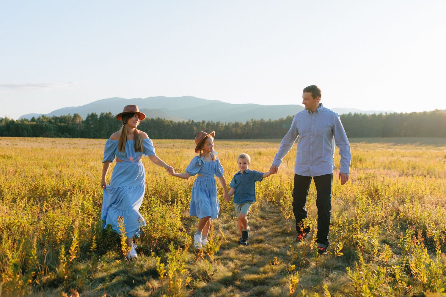 A couple walks hand in hand through a golden wheat field at sunset with lens flare in the background.