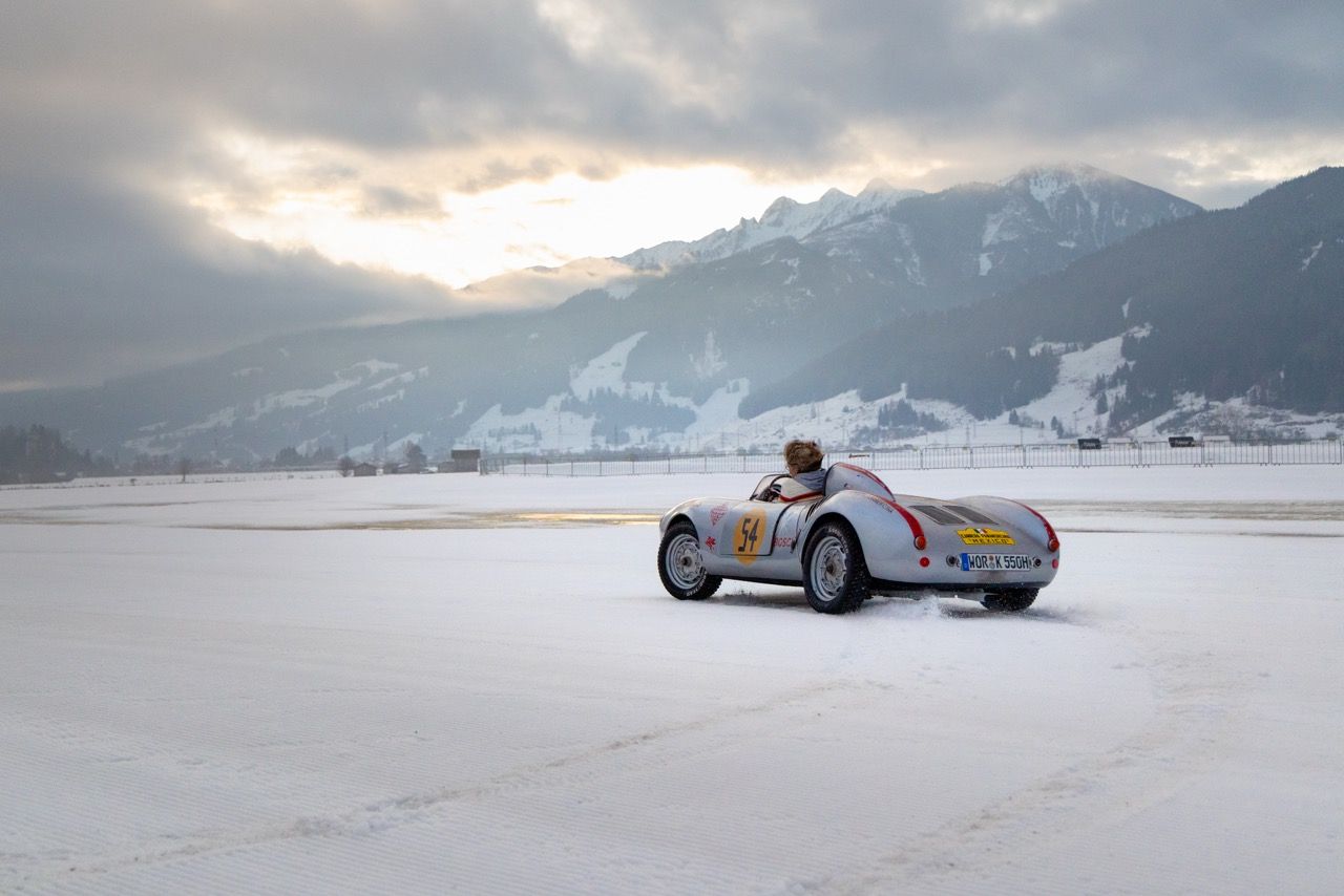 Vintage silver race car on a snow-covered track with mountain backdrop.