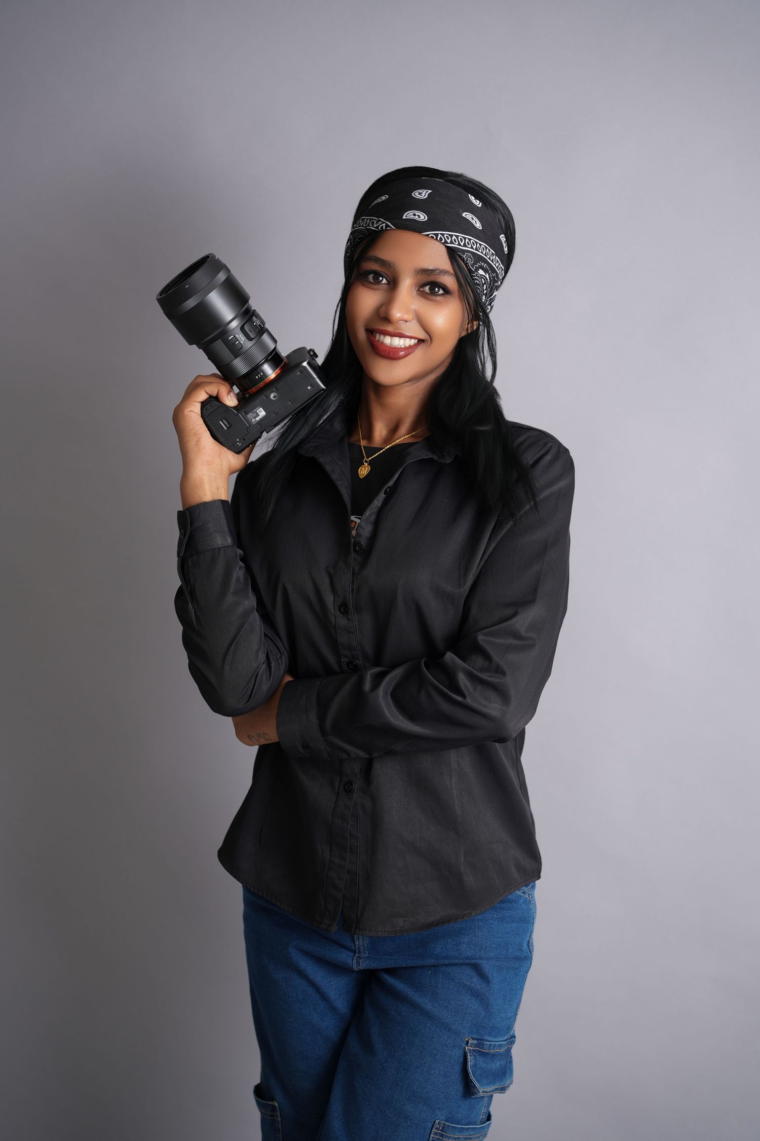 Photographer wearing a black hoodie and blue jeans poses with professional camera equipment in creative studio angles.