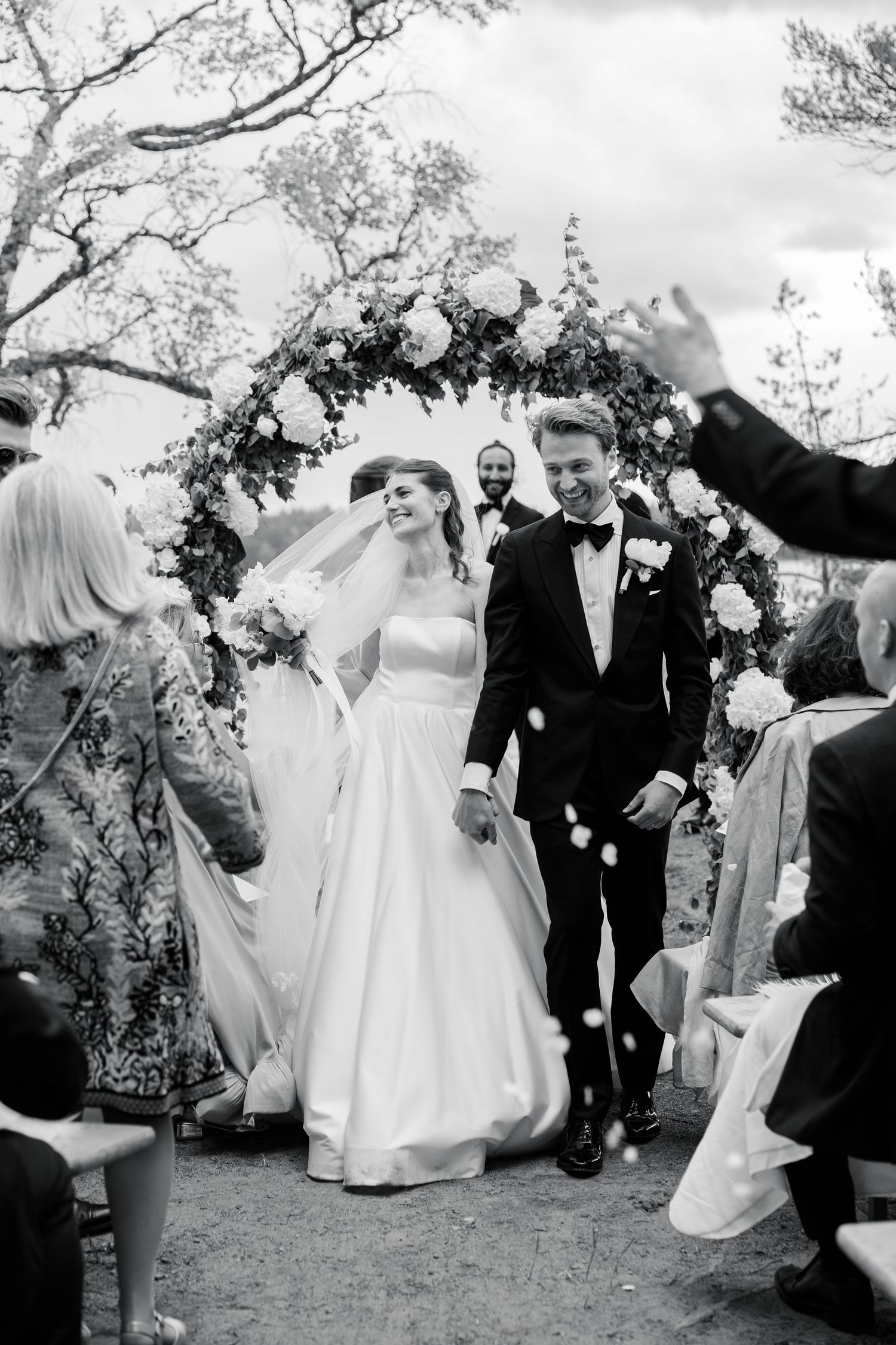 A wedding scene outside a grand yellow manor house with figures walking on gravel courtyard at sunset.