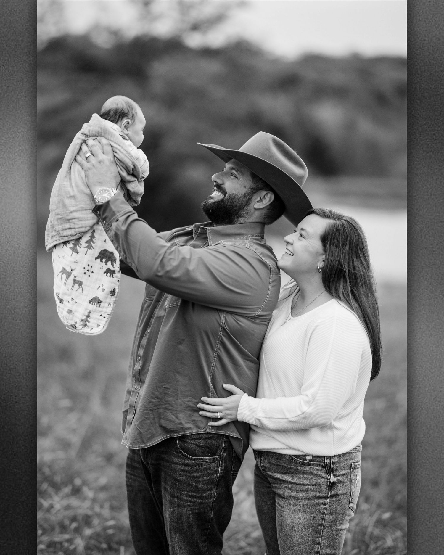 A couple shares a joyful moment lifting and playing with a small baby in a series of black and white outdoor photos.