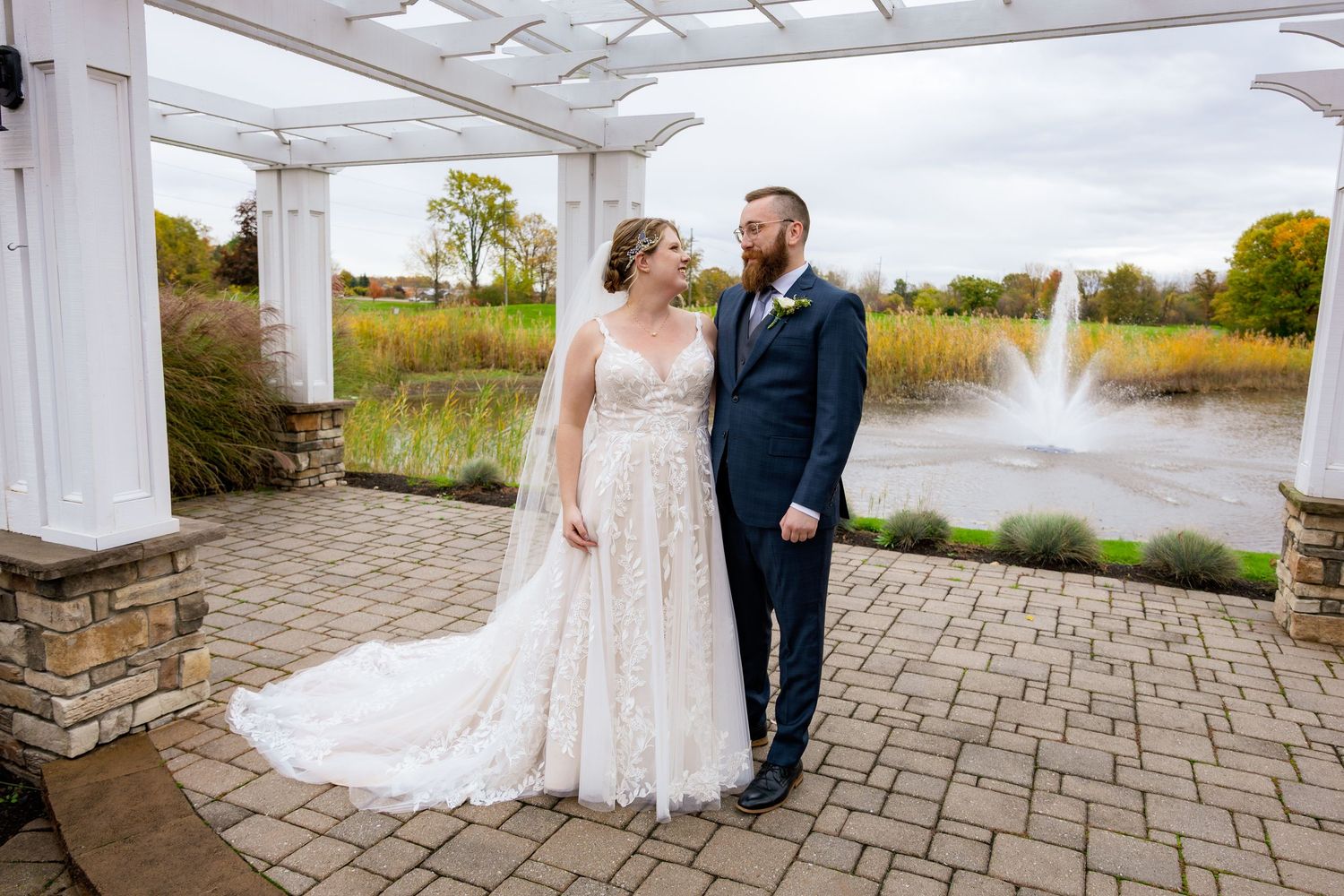 Wedding ceremony takes place under a rustic wooden pavilion with exposed beams and scenic view through archway in background.