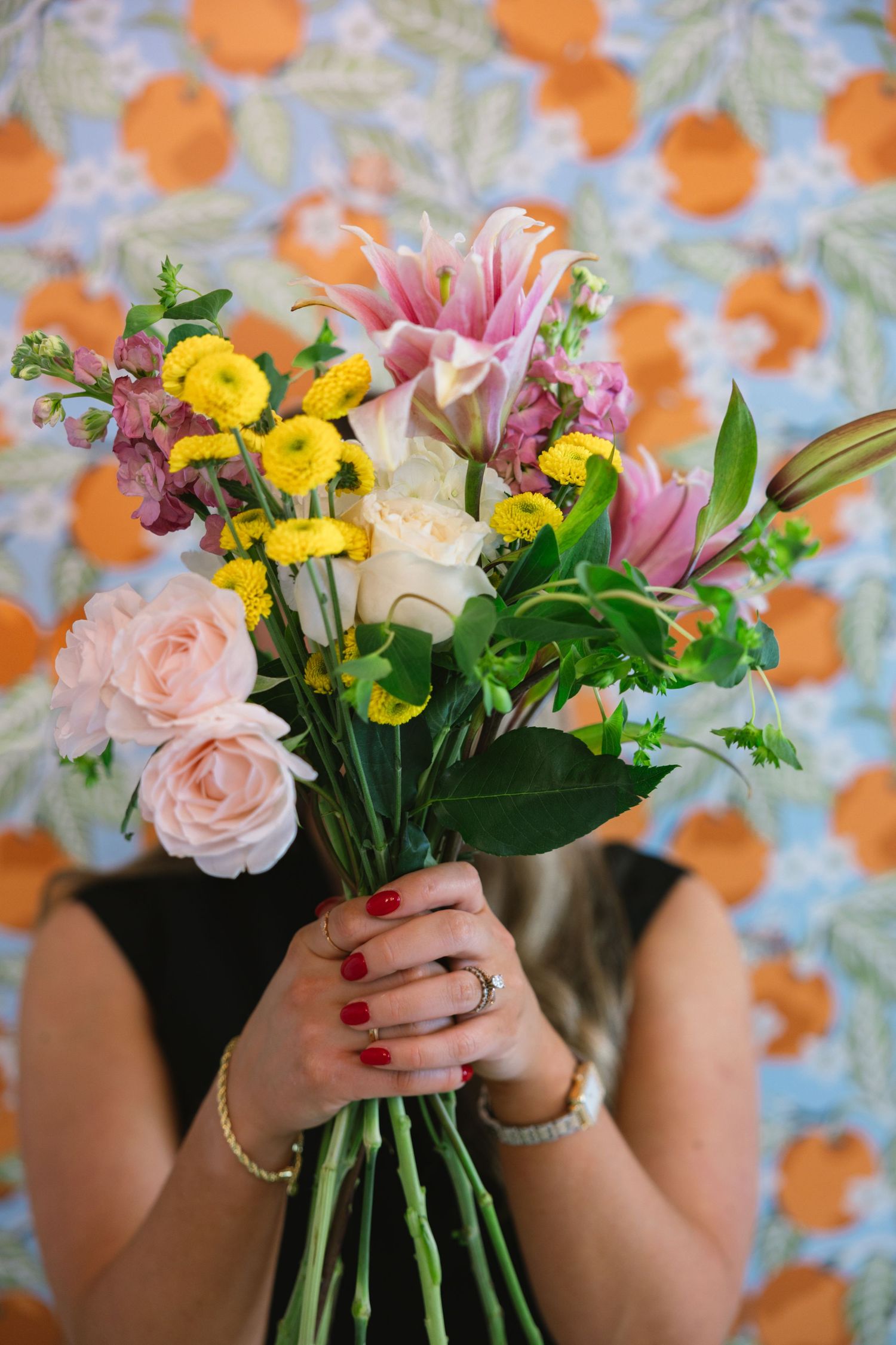 Fresh spring bouquet with pink roses, yellow flowers and lilies shown being arranged against an orange patterned background. East Tennessee