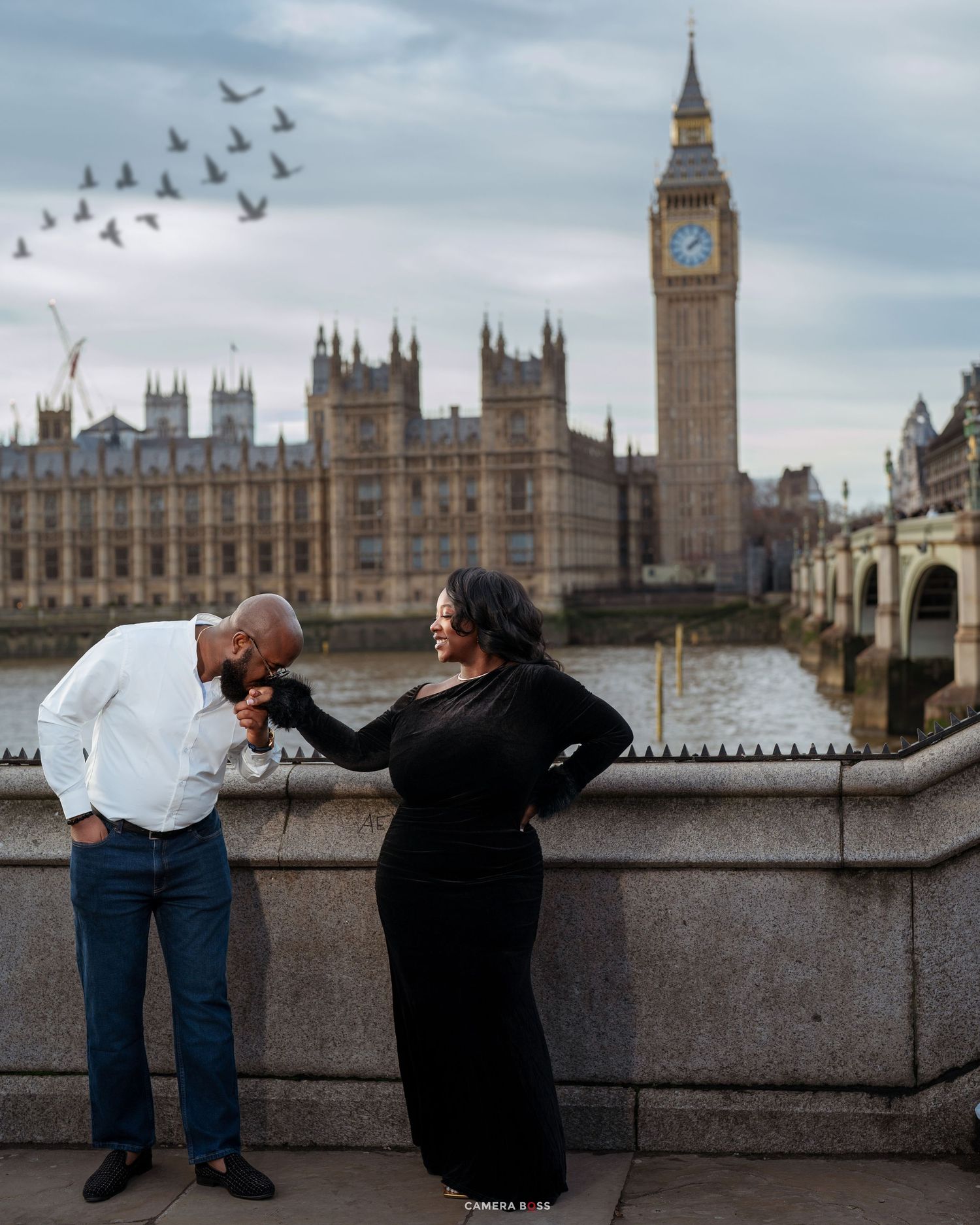 Two tourists lean over the stone wall of Westminster Bridge to admire views of the River Thames and Houses of Parliament in London.