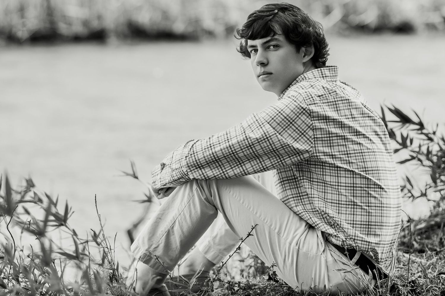 A black and white portrait of someone reclining in casual attire outdoors.