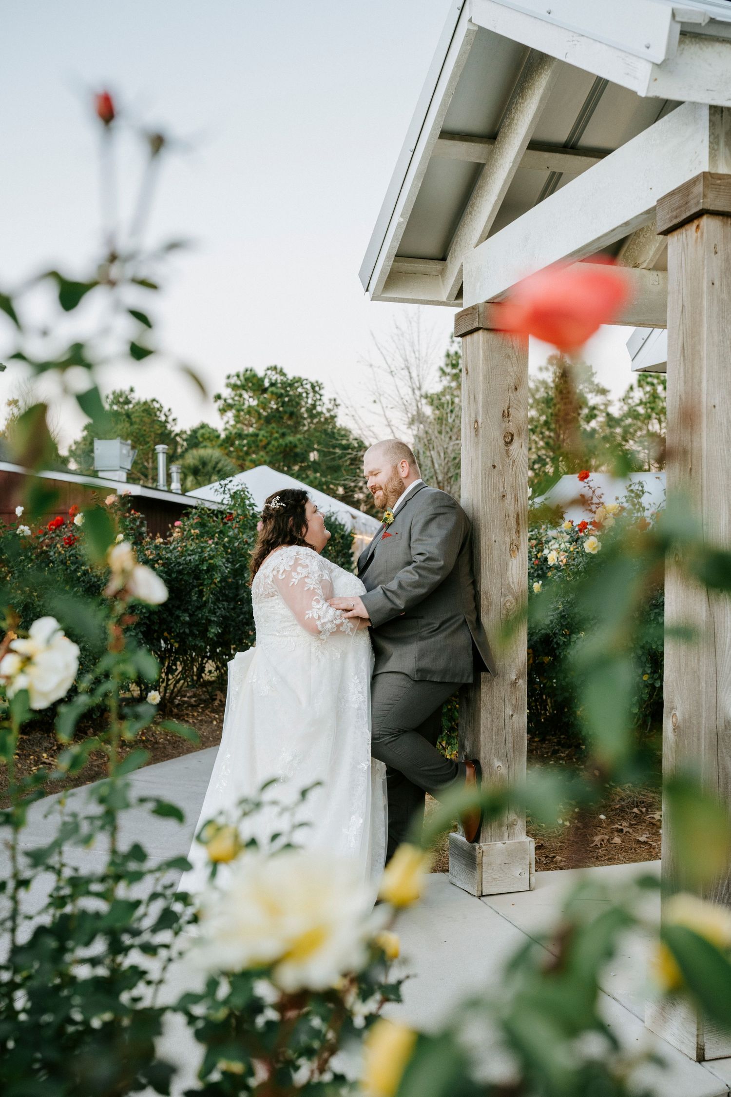 A romantic wedding moment captured in a garden setting with white pillars and blooming flowers in the foreground.