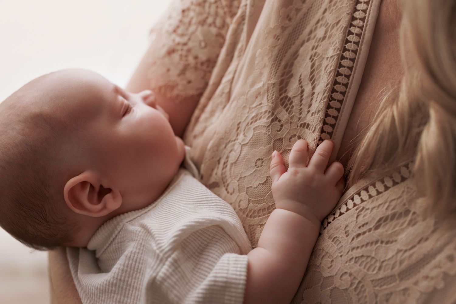 Infant in white knit sweater holding onto cream-colored cable knit fabric while nursing.