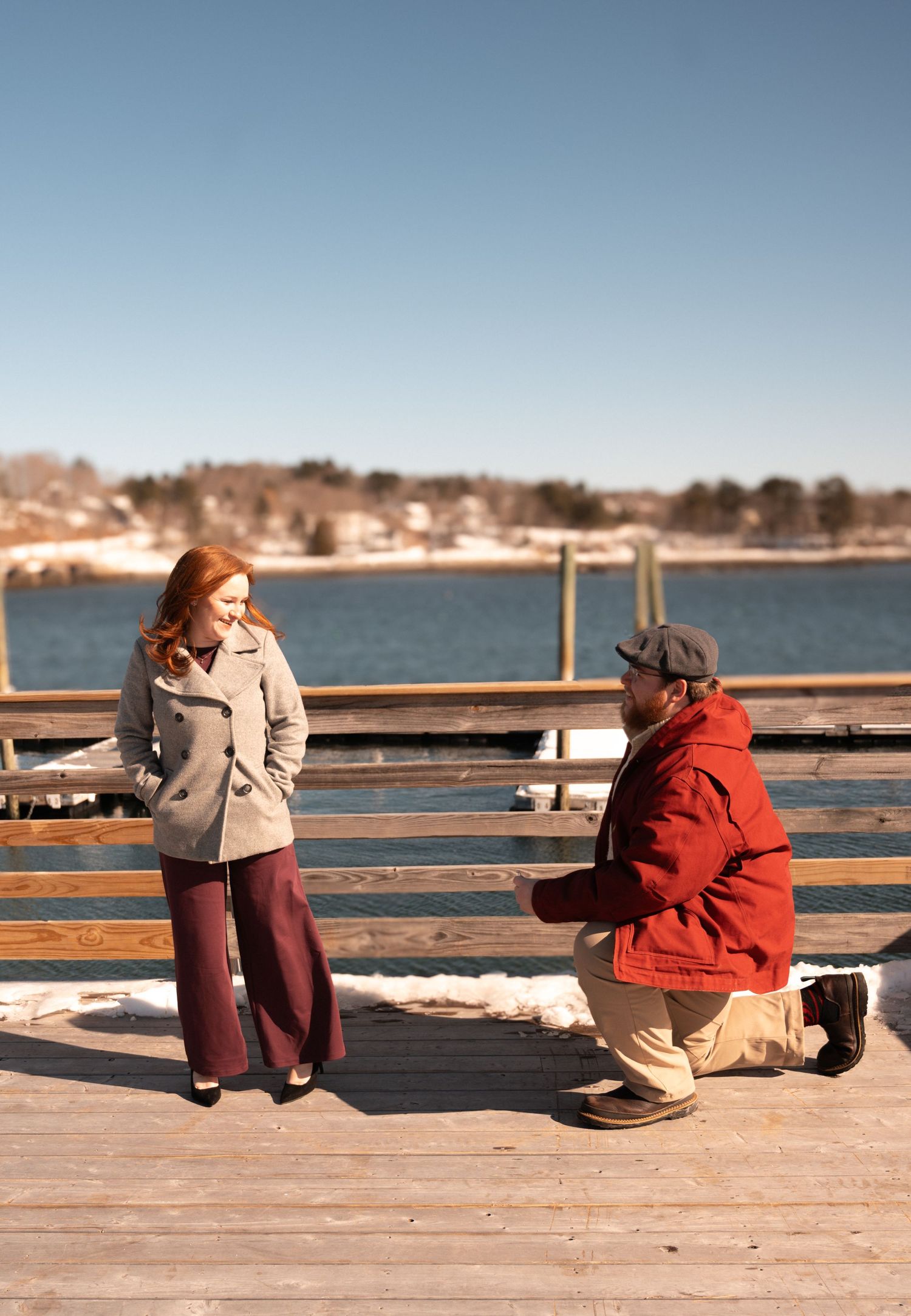 Couple sits together on a wooden dock by the water on a sunny day.