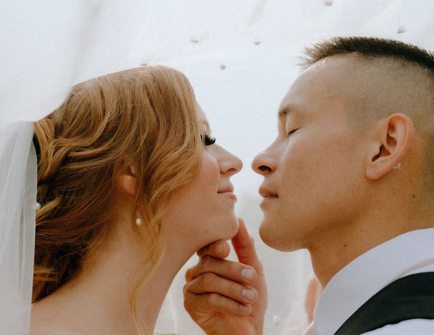An intimate romantic moment shared between partners under a delicate white veil.