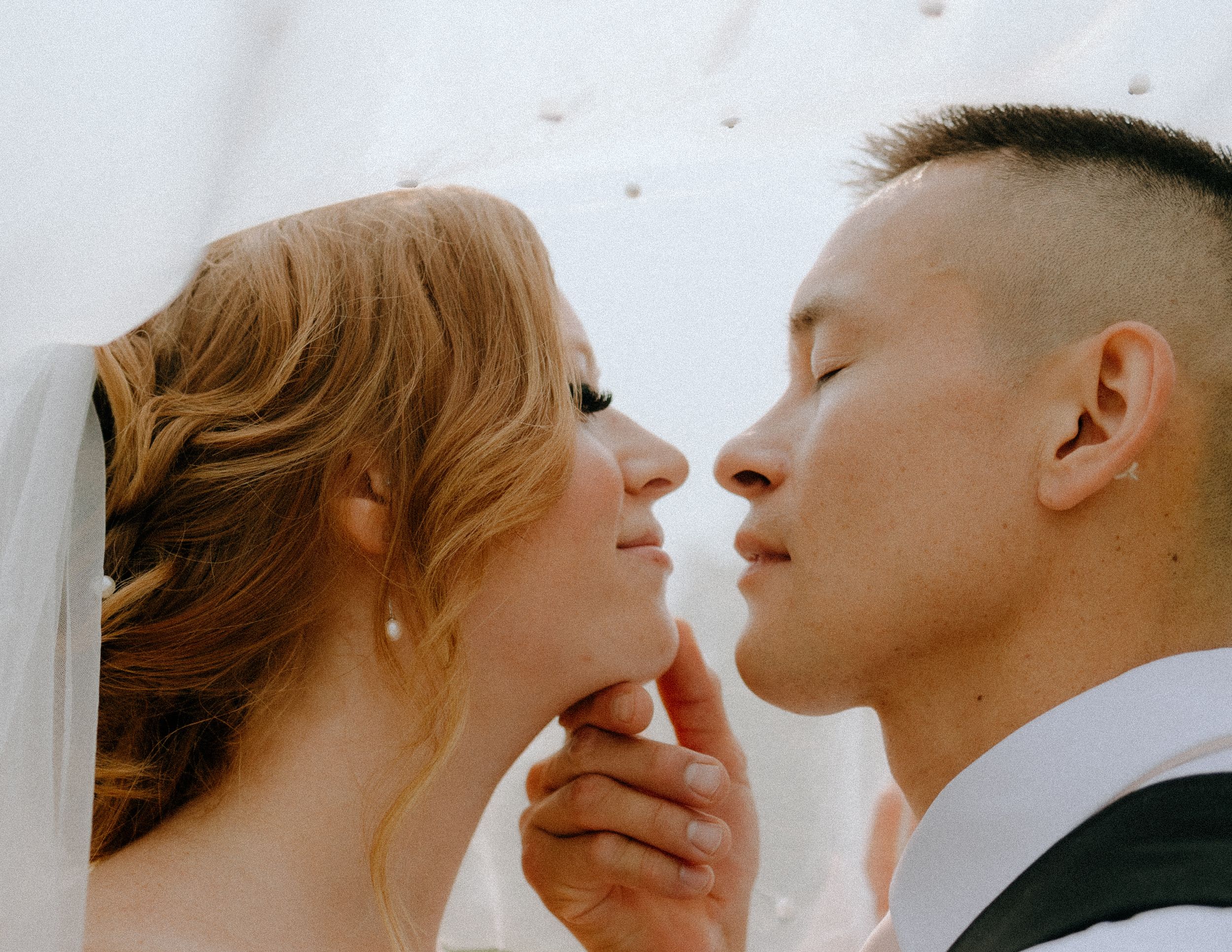 An intimate romantic moment shared between partners under a delicate white veil.
