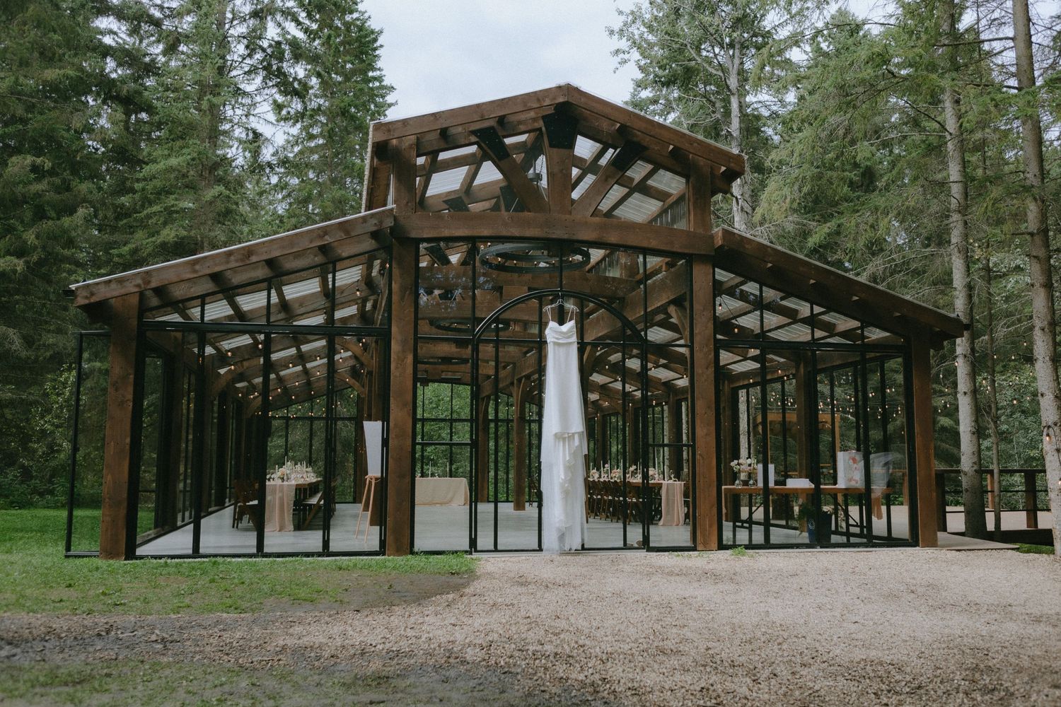 A modern glass and wood wedding pavilion surrounded by evergreen forest.