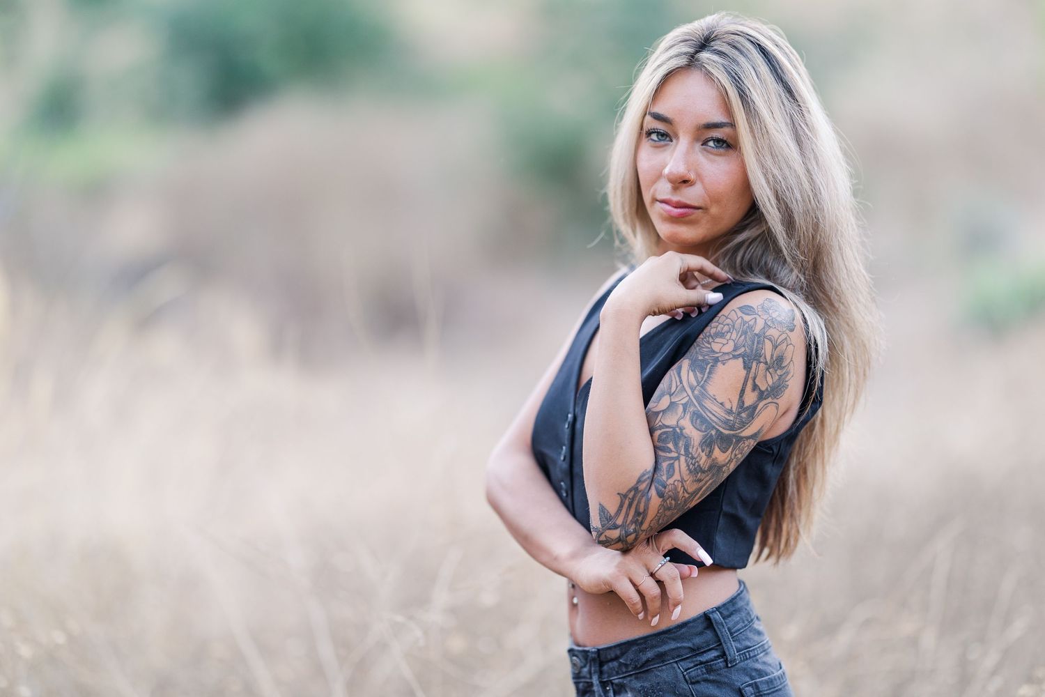 Portrait in tall grass field featuring casual attire and visible tattoo artwork.