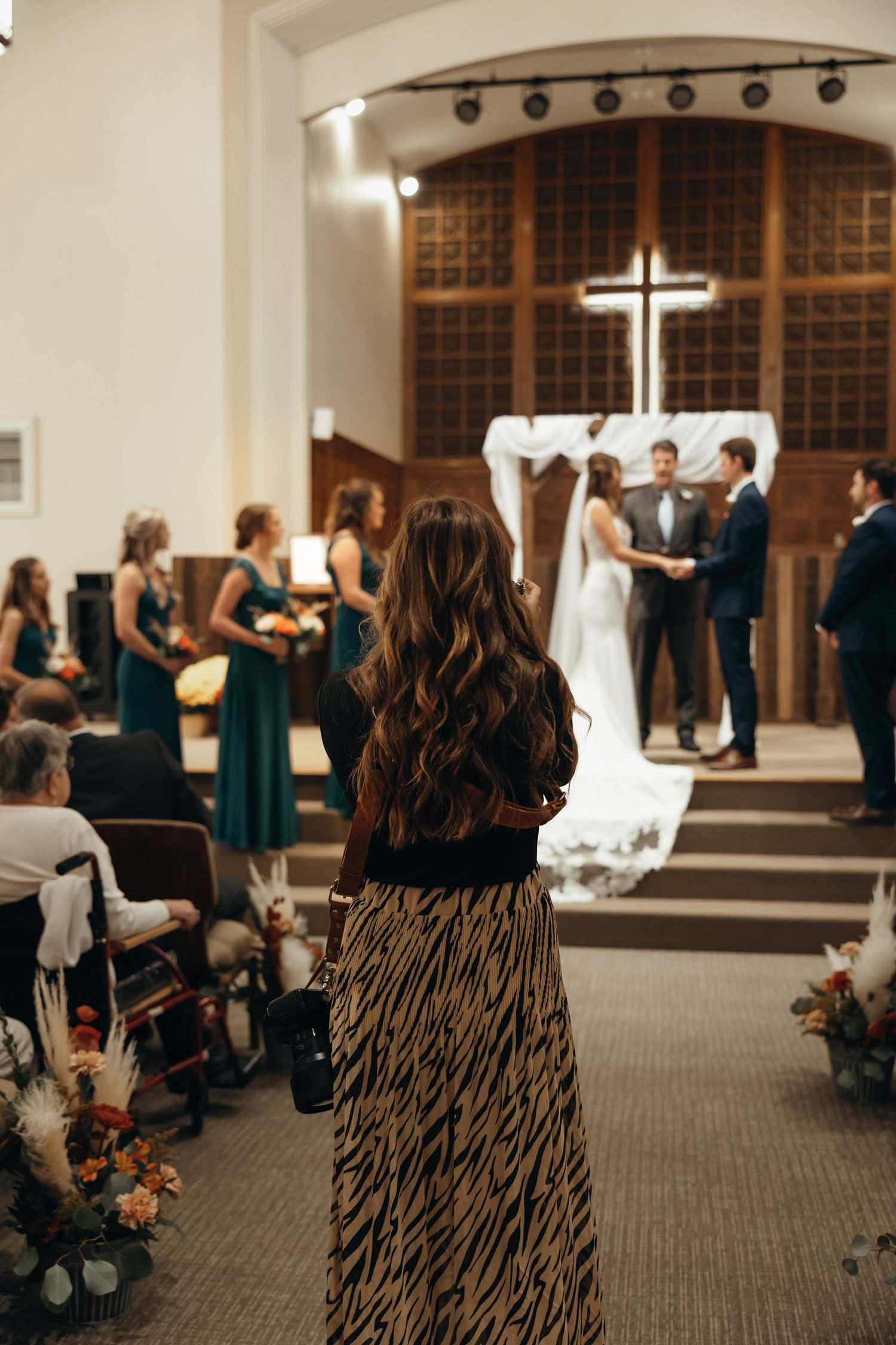 Wedding ceremony in progress at modern church with cross and guests in attendance.