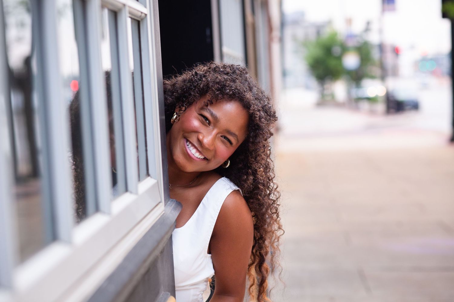 A radiant smile lights up a sidewalk scene along storefronts on a bright day.