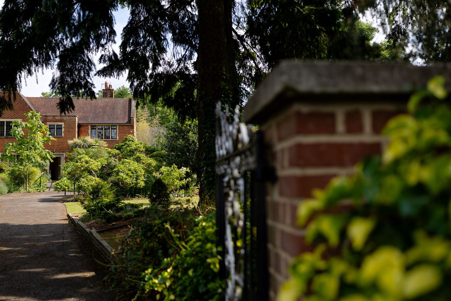 A winding garden path leads through colorful flower beds and lush landscaping to a brick house entrance.
