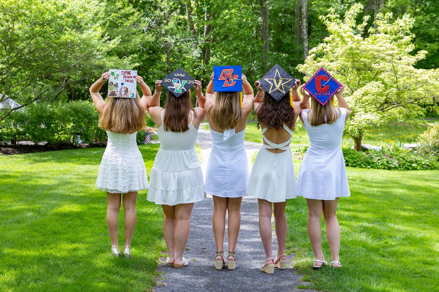 Group of graduates in bright blue robes showing off their decorated mortarboard caps outside a brick building.