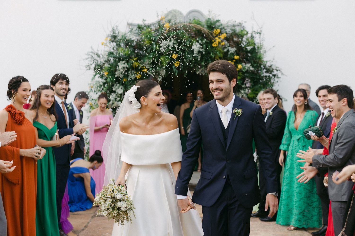 A happy wedding party celebrates with laughter and joy during an outdoor celebration in lush greenery.