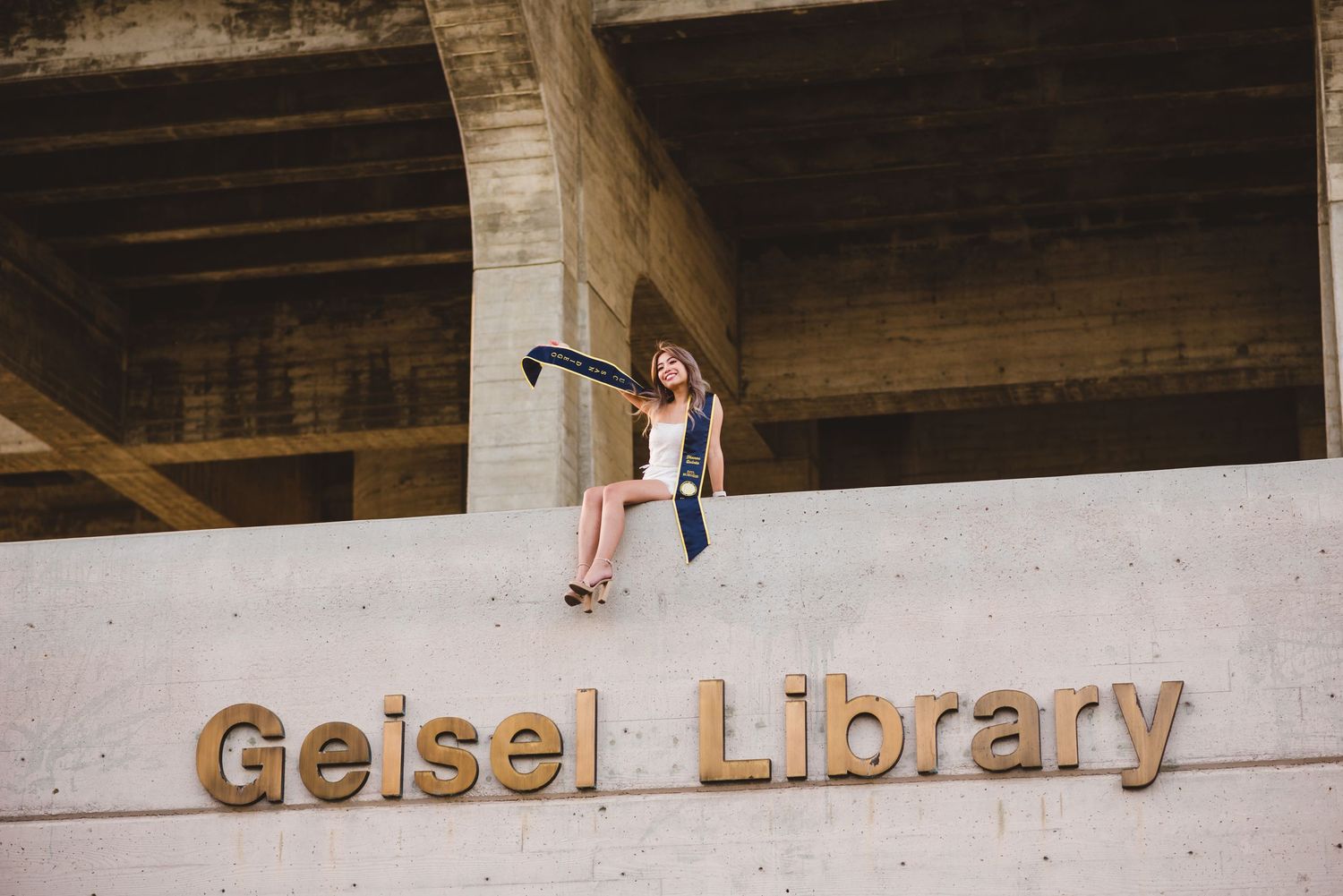 UCSD graduate sitting on top of the ledge at Geisel Library to pose for a grad photo.