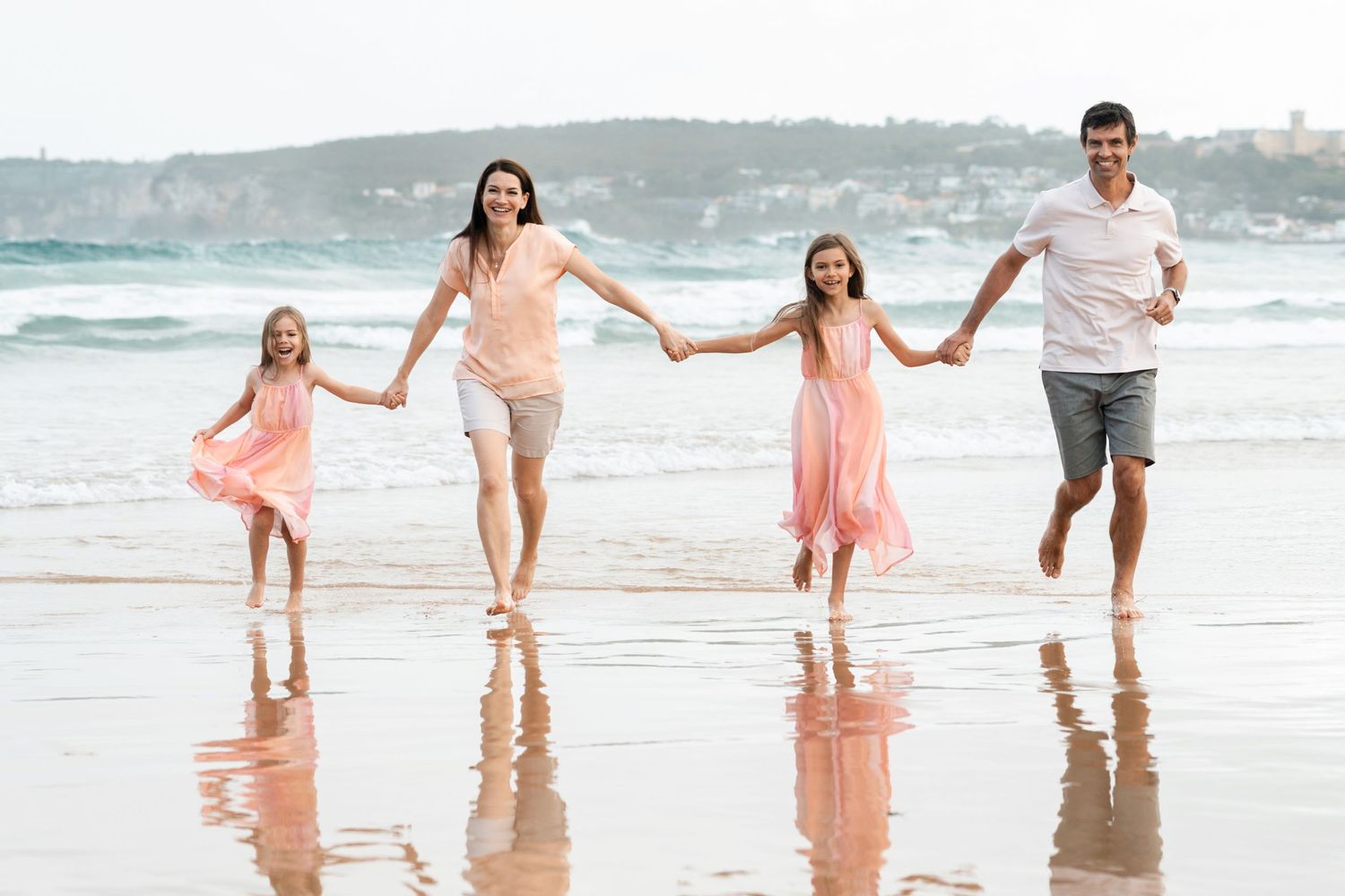 Family Mom, Dad and two daughters in the same colour dress walking in the water towards a family photographer in Northern Beaches Freshwater