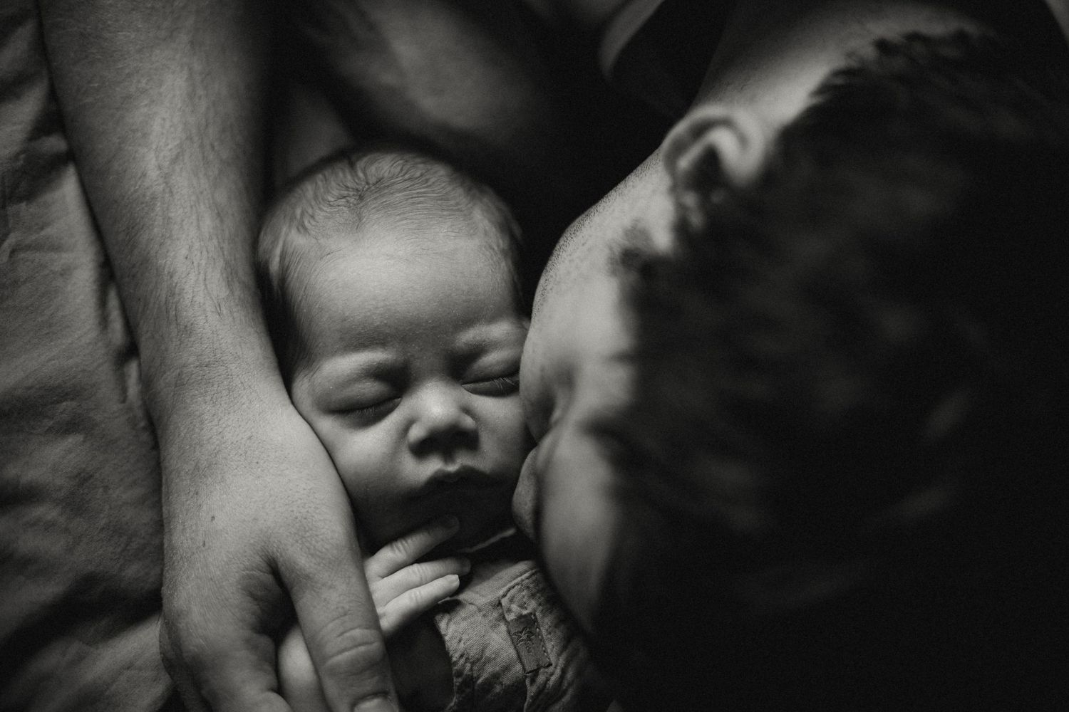 Black and white intimate portrait showing a sleeping infant being held lovingly by adult hands.