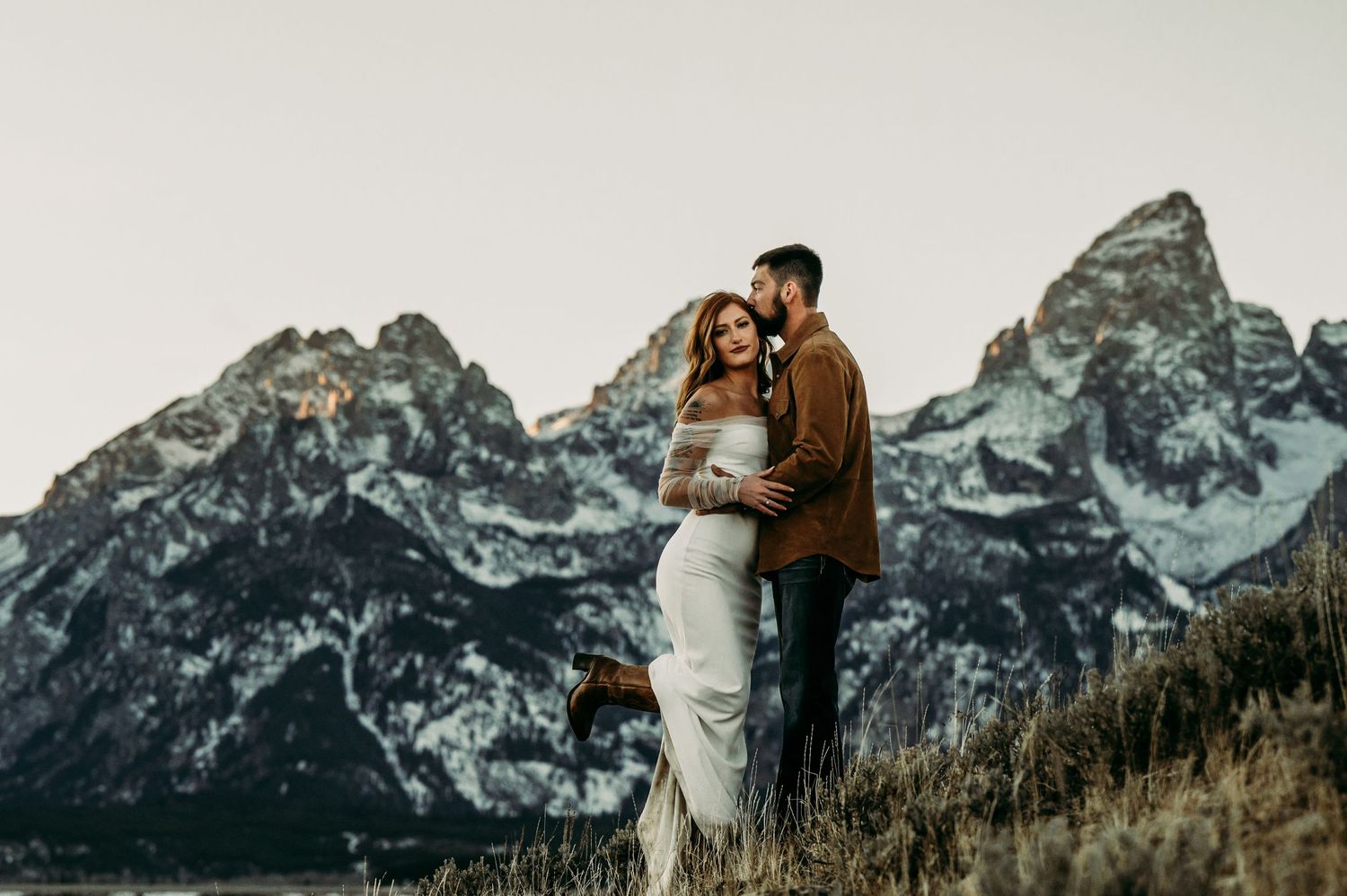 A romantic embrace captured against towering mountain peaks at sunset.