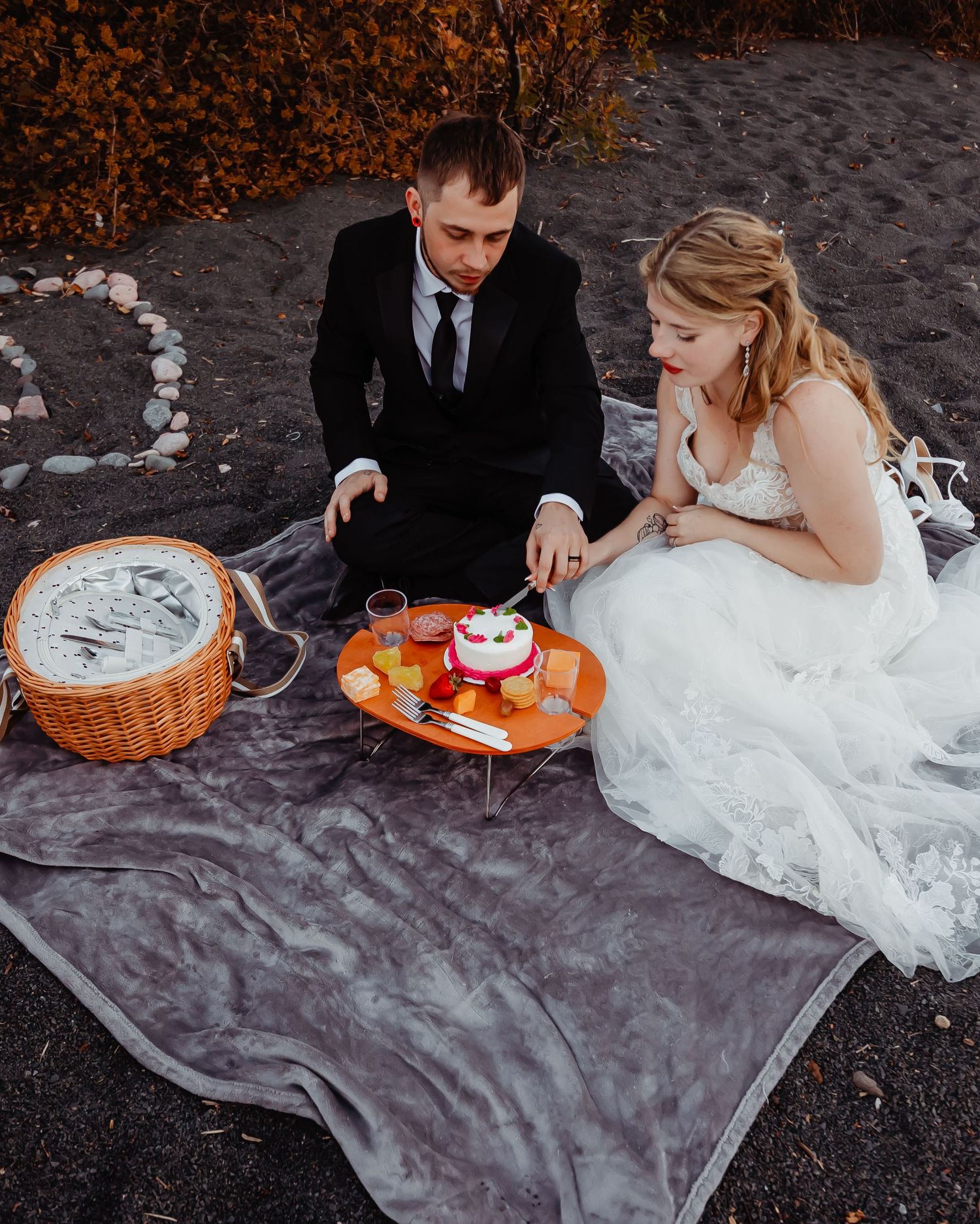 A wedding couple enjoys a picnic on a blanket with a wicker basket.