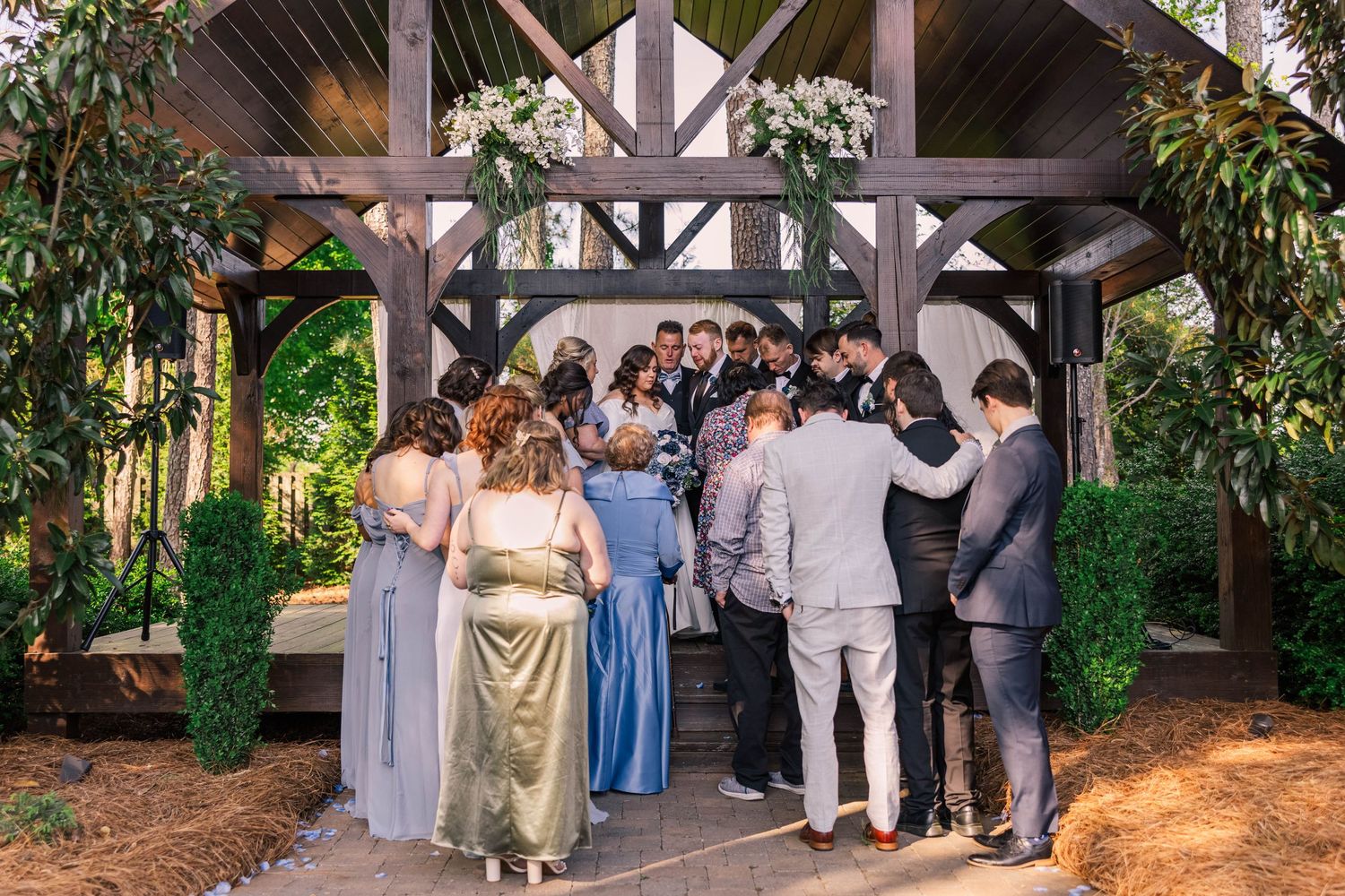 Wedding guests gathered under wooden pavilion decorated with greenery.