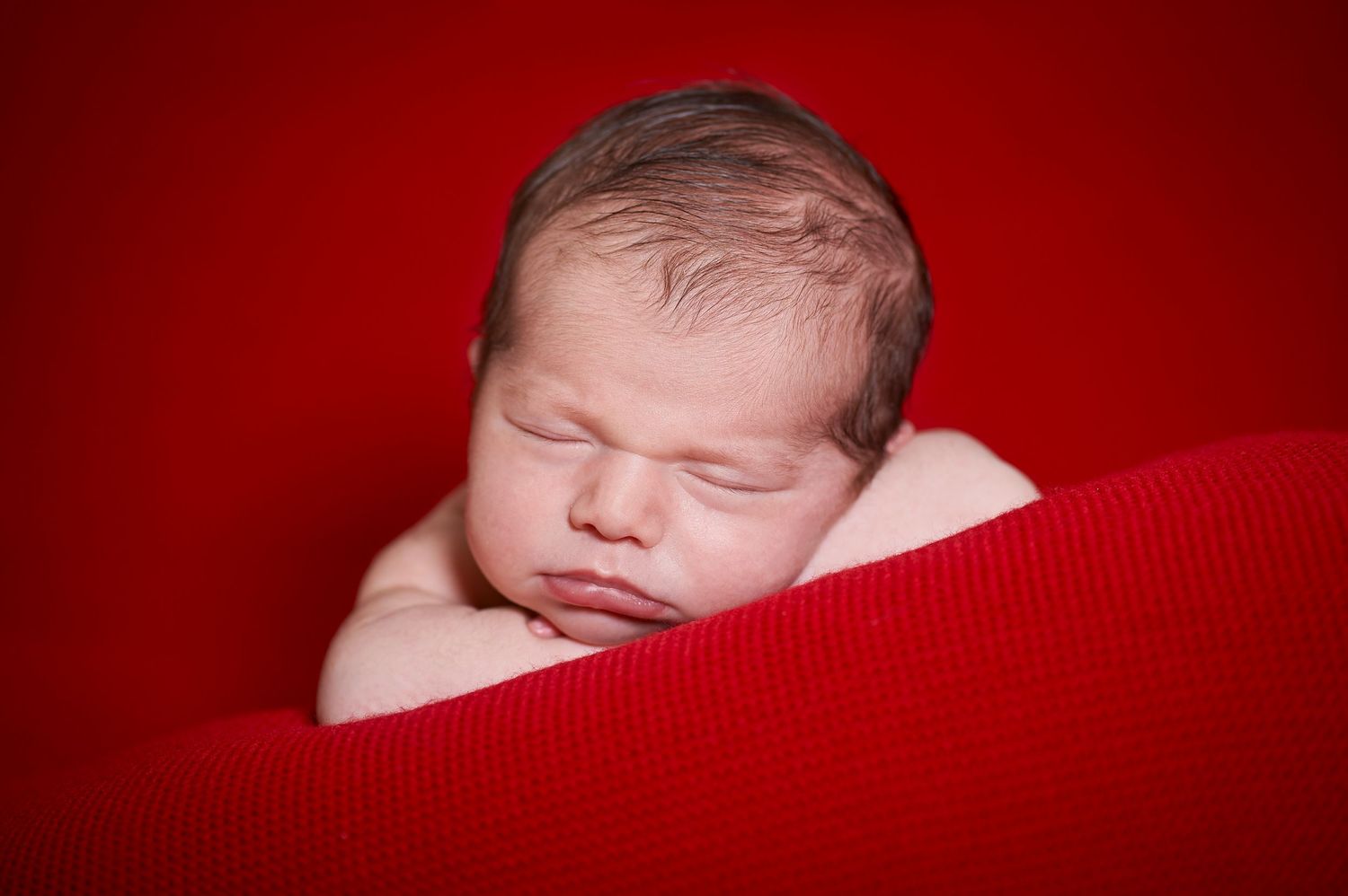 Peaceful newborn baby sleeping on a soft red knit blanket.