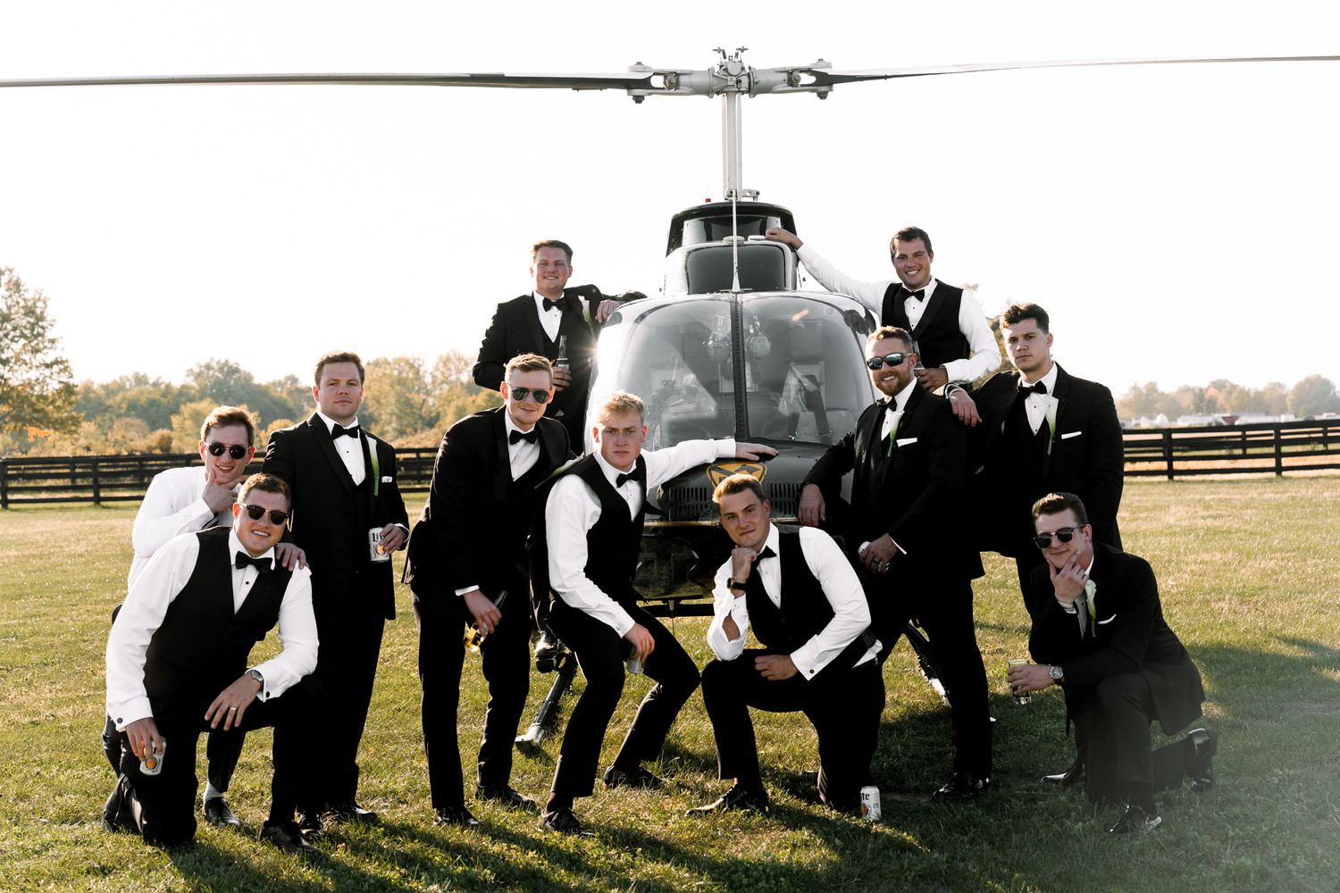 Groomsmen strike fun poses in front of a military helicopter in formal attire.