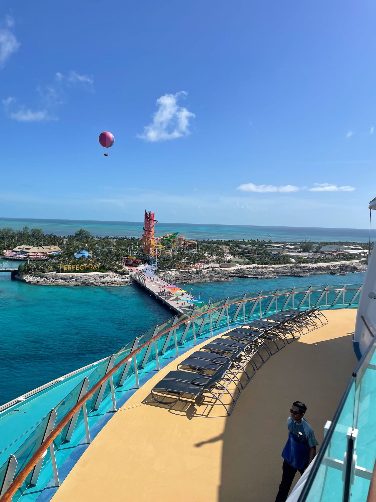 A cruise ship deck overlooking bright turquoise waters and a coastal lighthouse under blue skies.