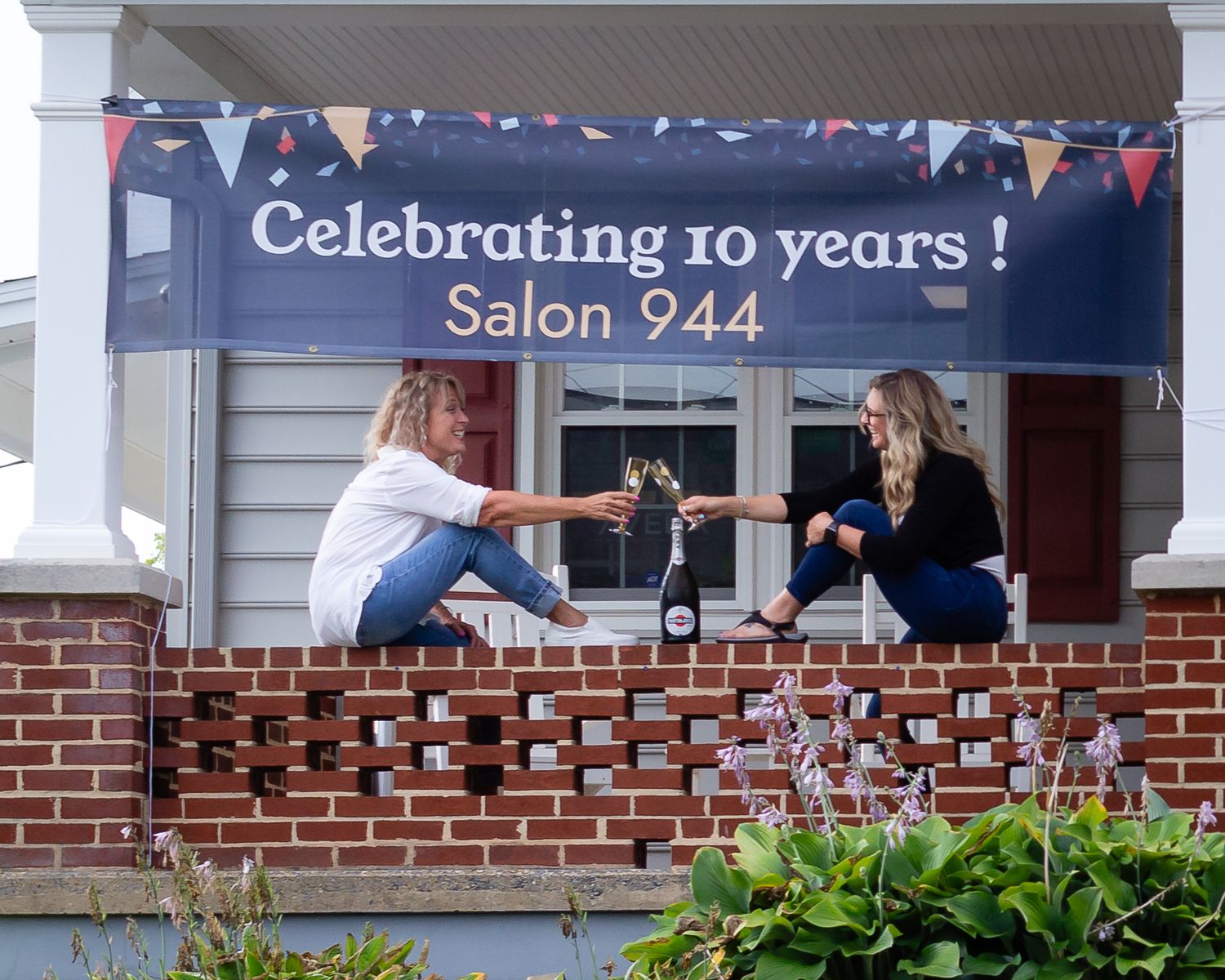 Two people toasting at outdoor celebration with banner for Salon 244's 10th anniversary.