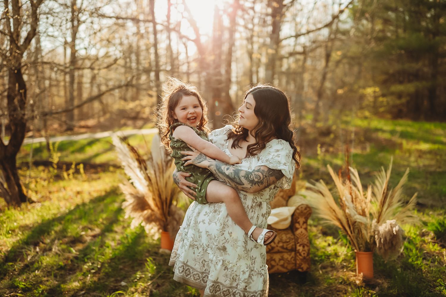 A tender outdoor family moment captured in golden sunlight among pampas grass and forest scenery.