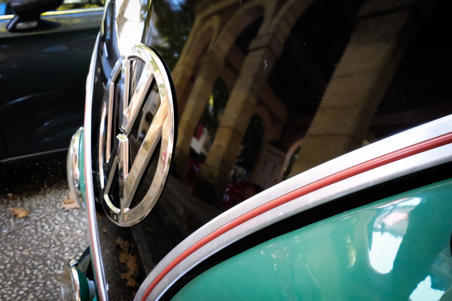 Close-up of a vintage Volkswagen Beetle logo on a two-tone black and green car with red pinstripe detail.