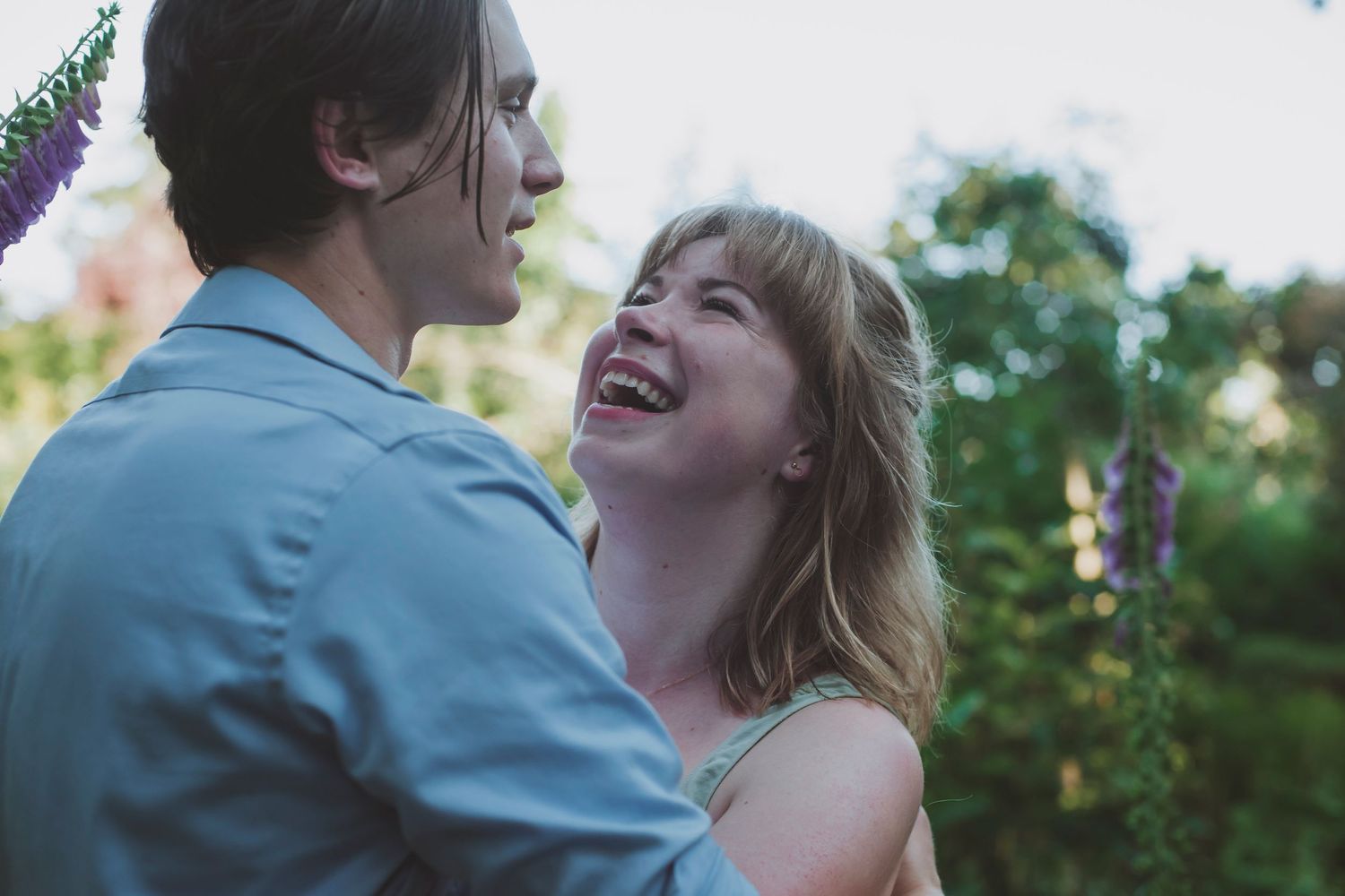 A young couple embraces and laughs together in a romantic outdoor garden setting during golden hour in Victoria, BC.