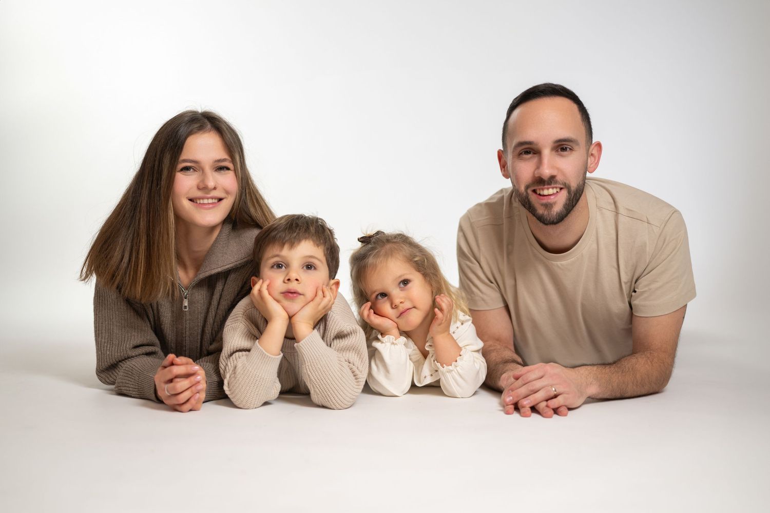 A family of four lies together on white background in casual attire for a studio portrait.