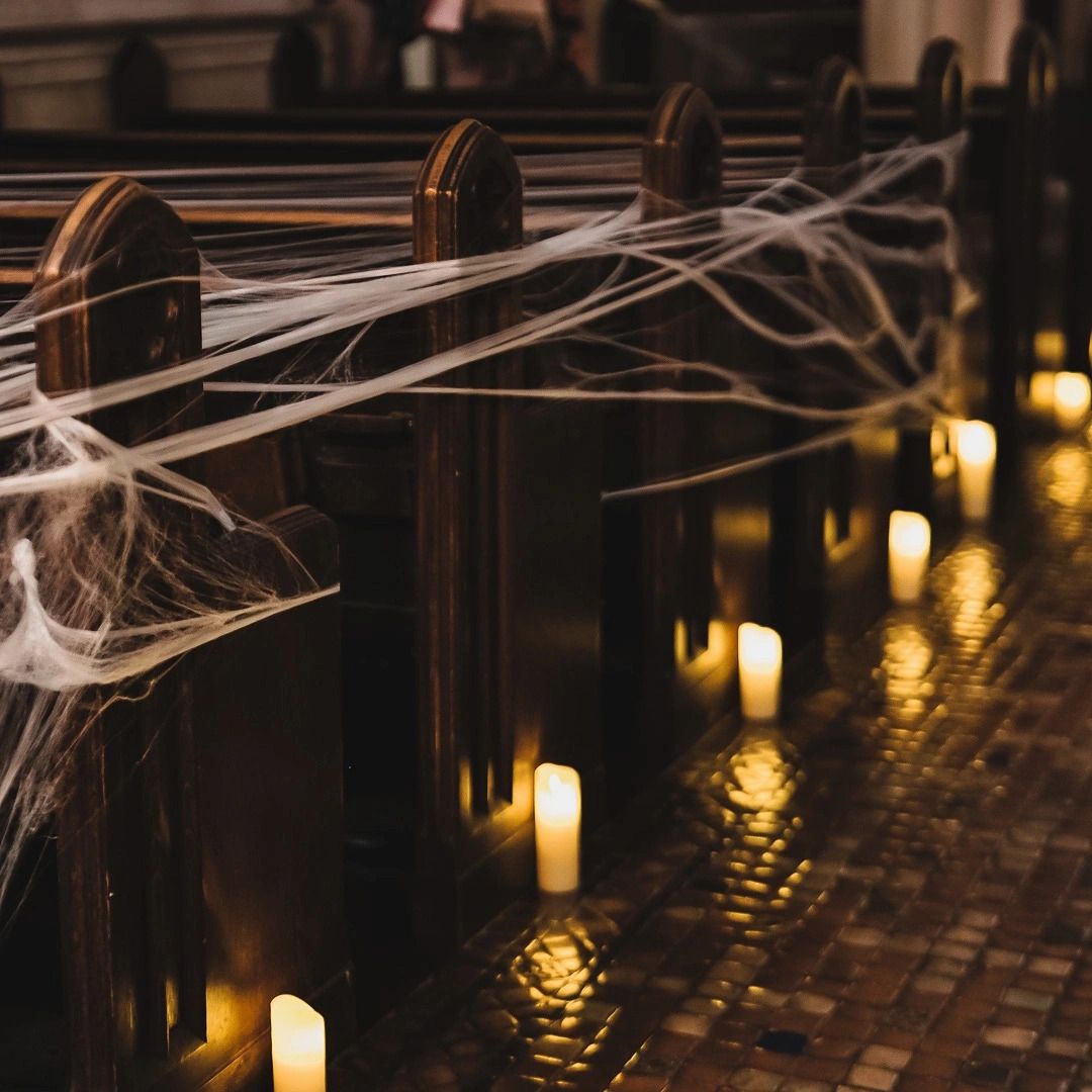 Multiple atmospheric candles flicker beside a paved path with spooky cobwebs creating a dark Halloween ambiance.