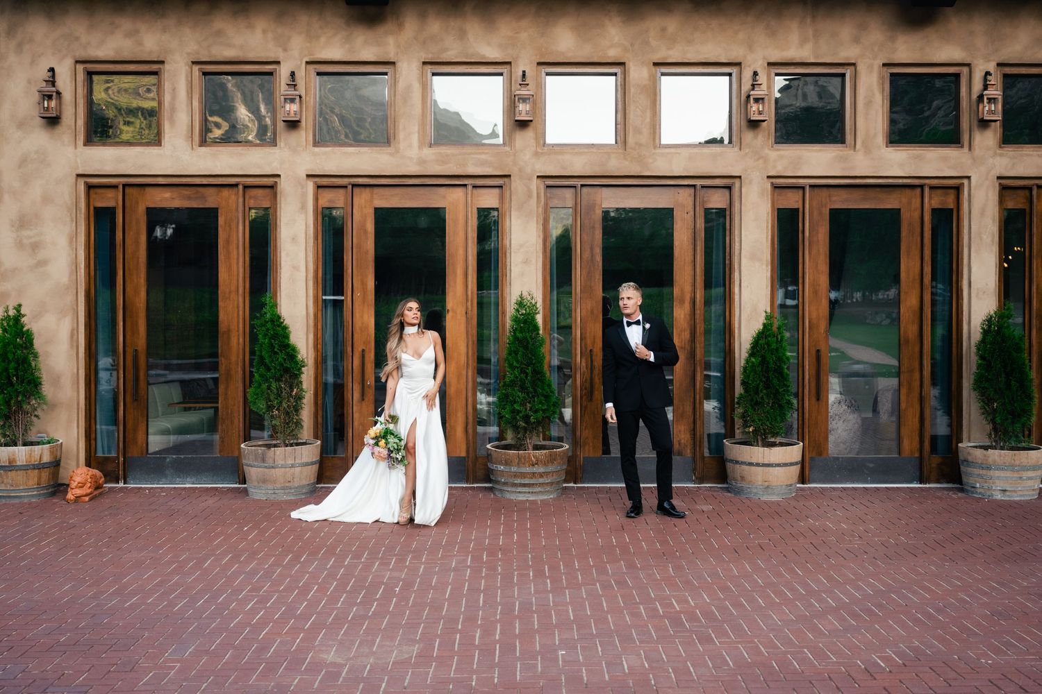 A bride and groom stand together during their wedding ceremony at an elegant brick courtyard with arched columns and greenery.