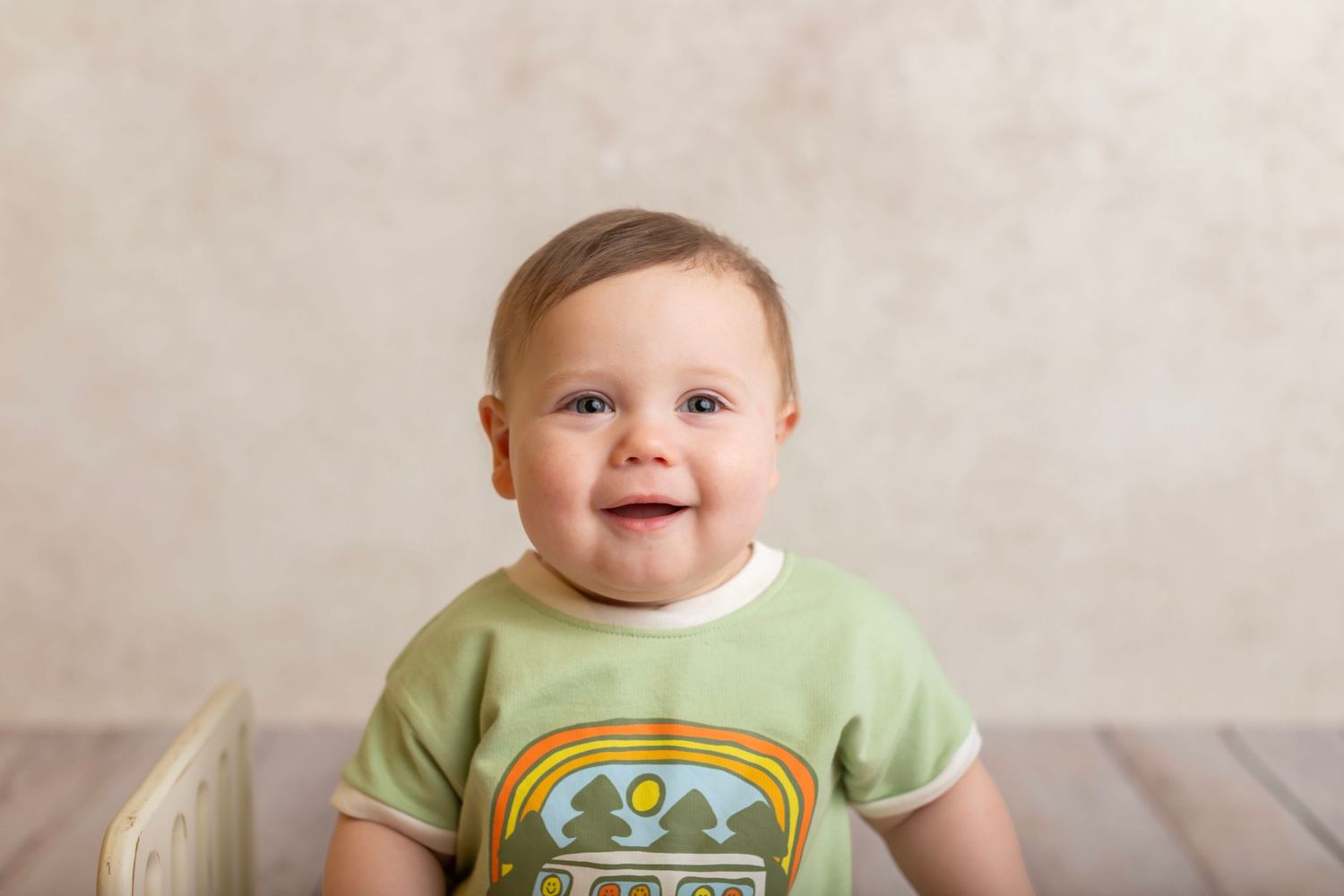 Baby in green t-shirt with camping design smiling at camera.