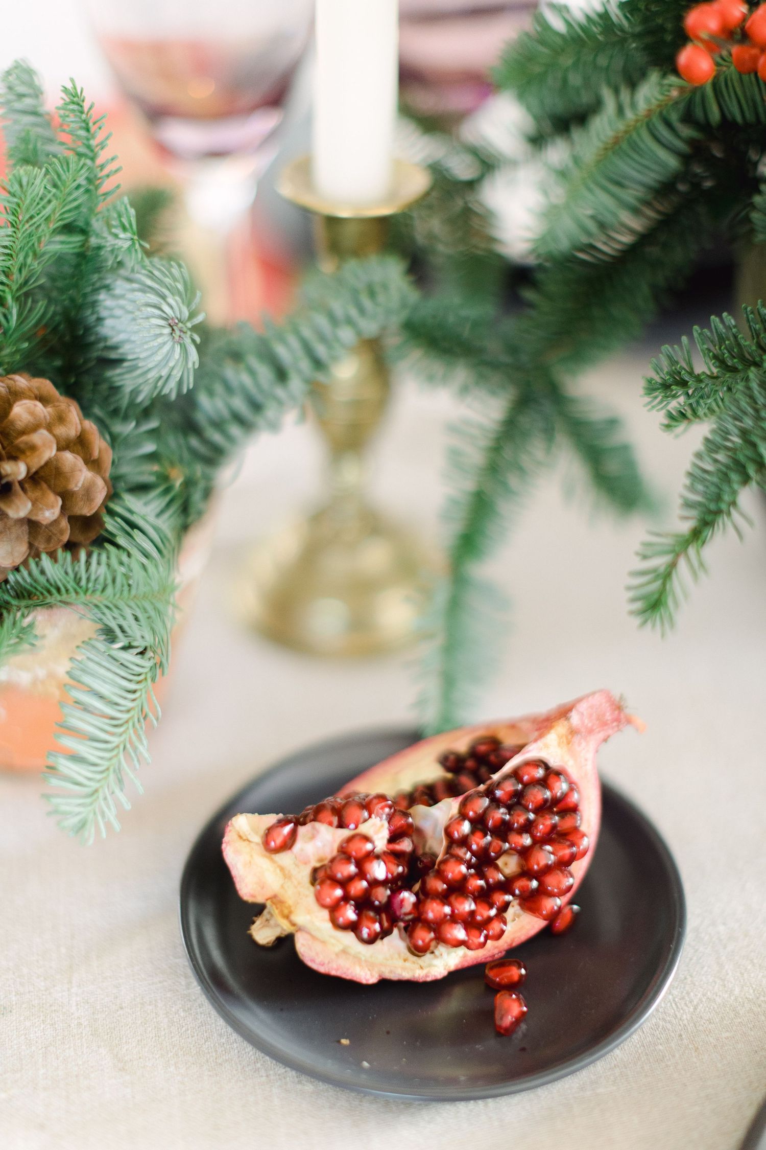 A sliced pomegranate on dark plate with evergreen branches and candle decor in background.