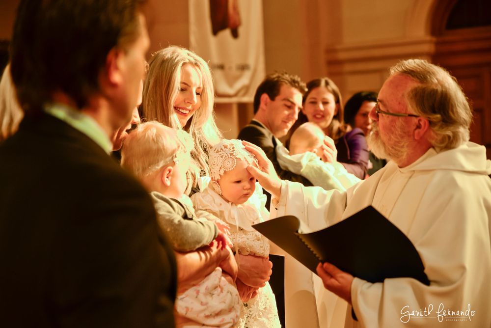 Priest blessing babies during a church baptism ceremony with smiling families gathered together.