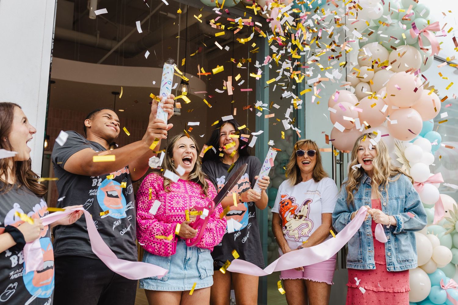 Group of friends celebrating with confetti cannons and balloons at a festive outdoor party event.